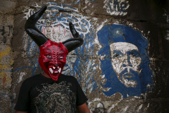 شخص يرتدى وجه الشيطان ويقف بجوار صورة جيفارا  -اليوم السابع -10 -2015