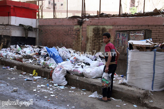 أحد الأطفال وهو يستعد لإلقاء القمامة بسور المدرسة -اليوم السابع -5 -2015