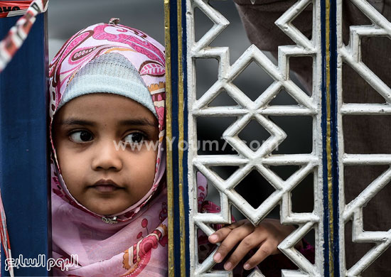 طفلة ماليزية تشاهد الصلاة من خلف الباب المعدنى للمسجد. -اليوم السابع -9 -2015