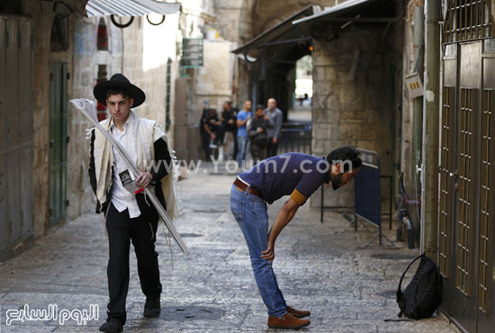 أحد المستوطنين فى طريقه إلى حائط البراق وفى جواره شاب فلسطينى يؤدى الصلاة فى الشارع  -اليوم السابع -9 -2015