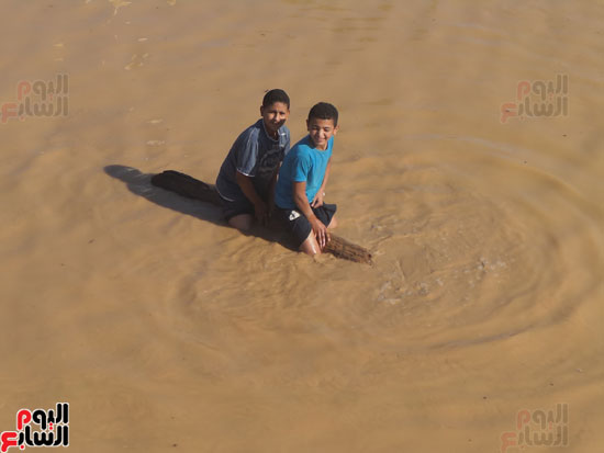 طفلان يركبان أحد جذوع النخيل داخل مياه السيول