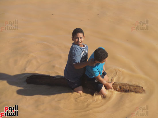 طفلان من القرية يركبون جذع نخلة للعبور بمياه السيول