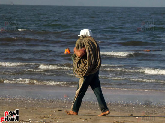 أحد الصيادين يحمل "حبال الشد" لوضعها بالمركب
