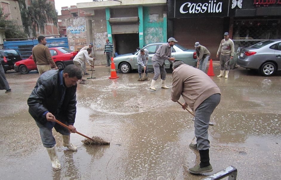عمال النظافة يكسحون مياه الأمطار من الشوارع