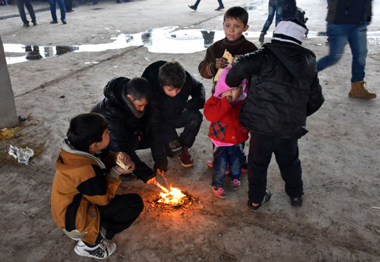 أطفال سوريين فروا من القصف يصطفون حول قطعة خشب مشتعلة للتدفئة