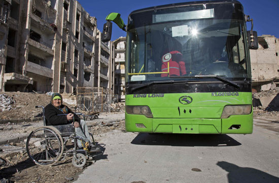 سيدة مسنة تنتظر حافلة خارجة من حلب