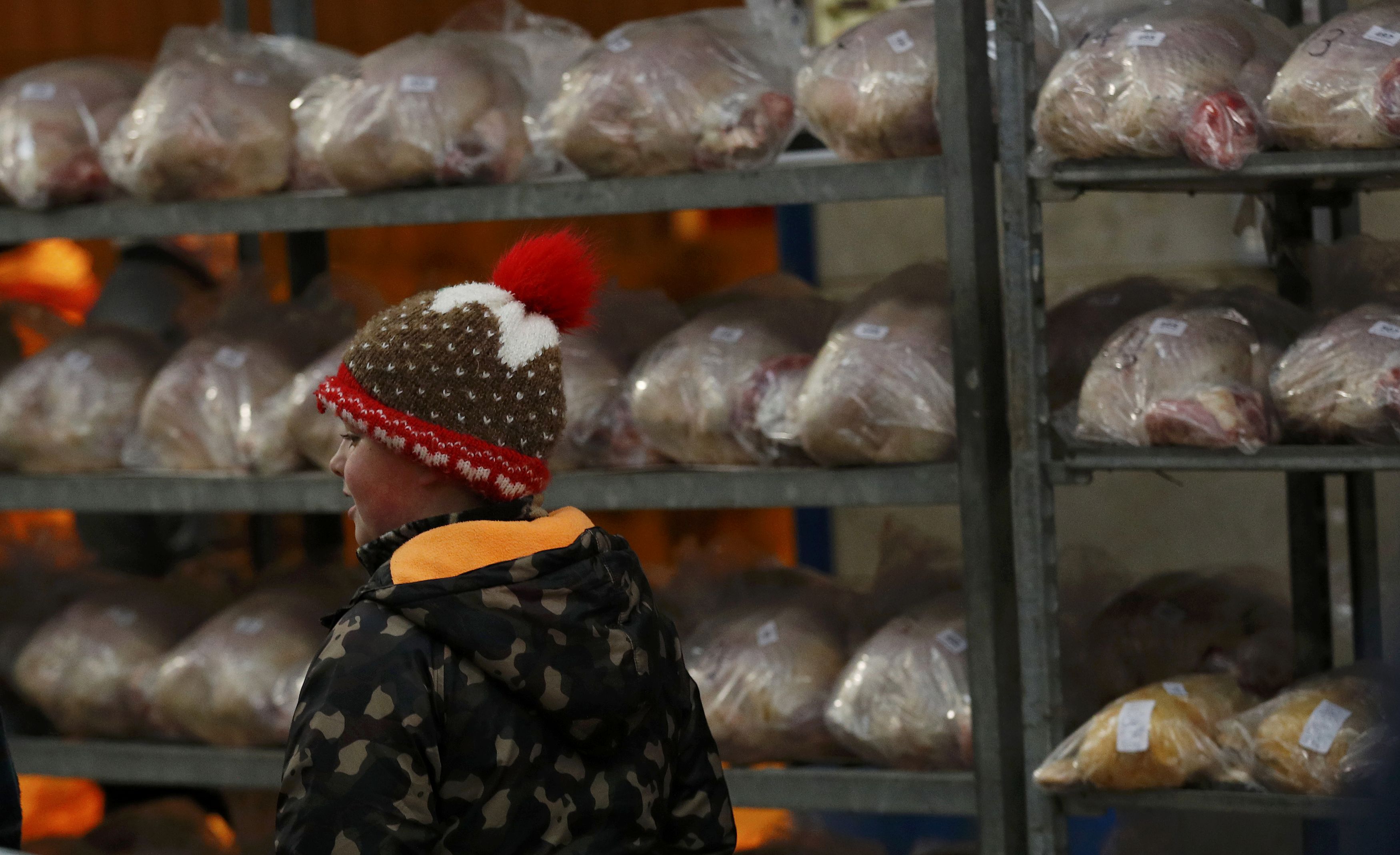 طفل يمر بجانب حاملة ديوك في مزاد لبيع الدواجن في مدينة تشلفرد البريطانية مع قرب الاحتفال بعيد الميلاد -رويترز