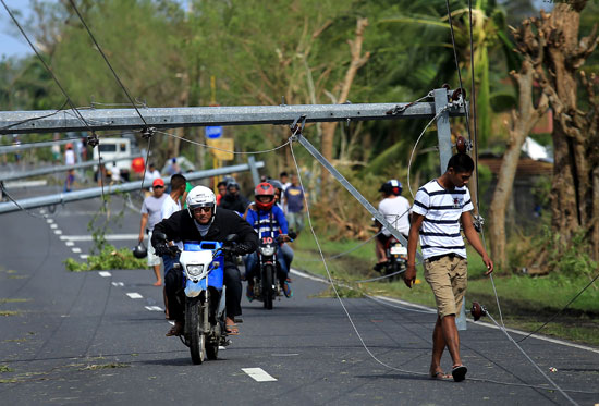 سائقى درجات يمرون أسفل عمود كهرباء سقط بعد أن ضرب الإعصار الفلبين 