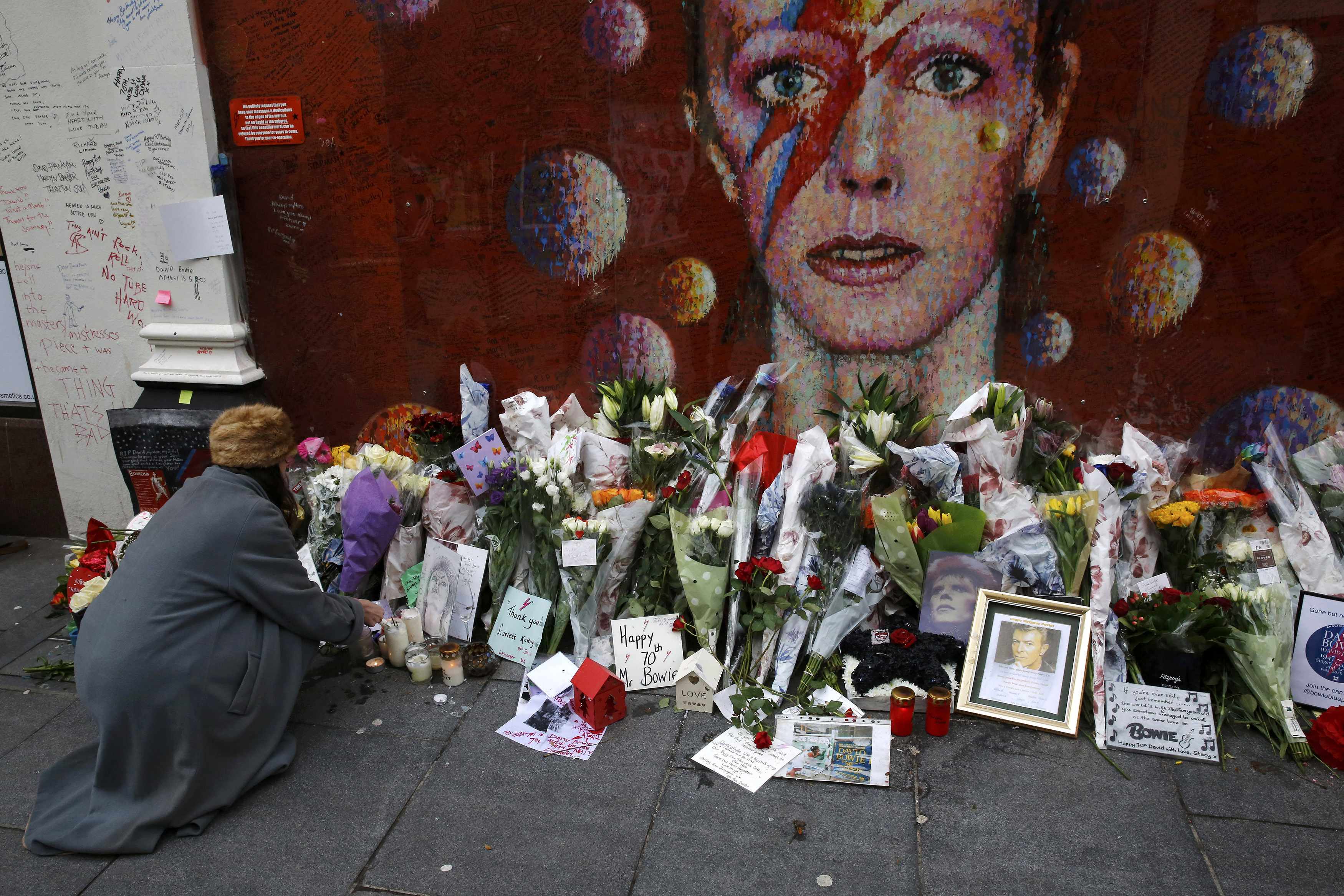 امرأة تضع الشموع بالقرب من لوحة جدارية لديفيد باوي في بريكستون جنوب لندن