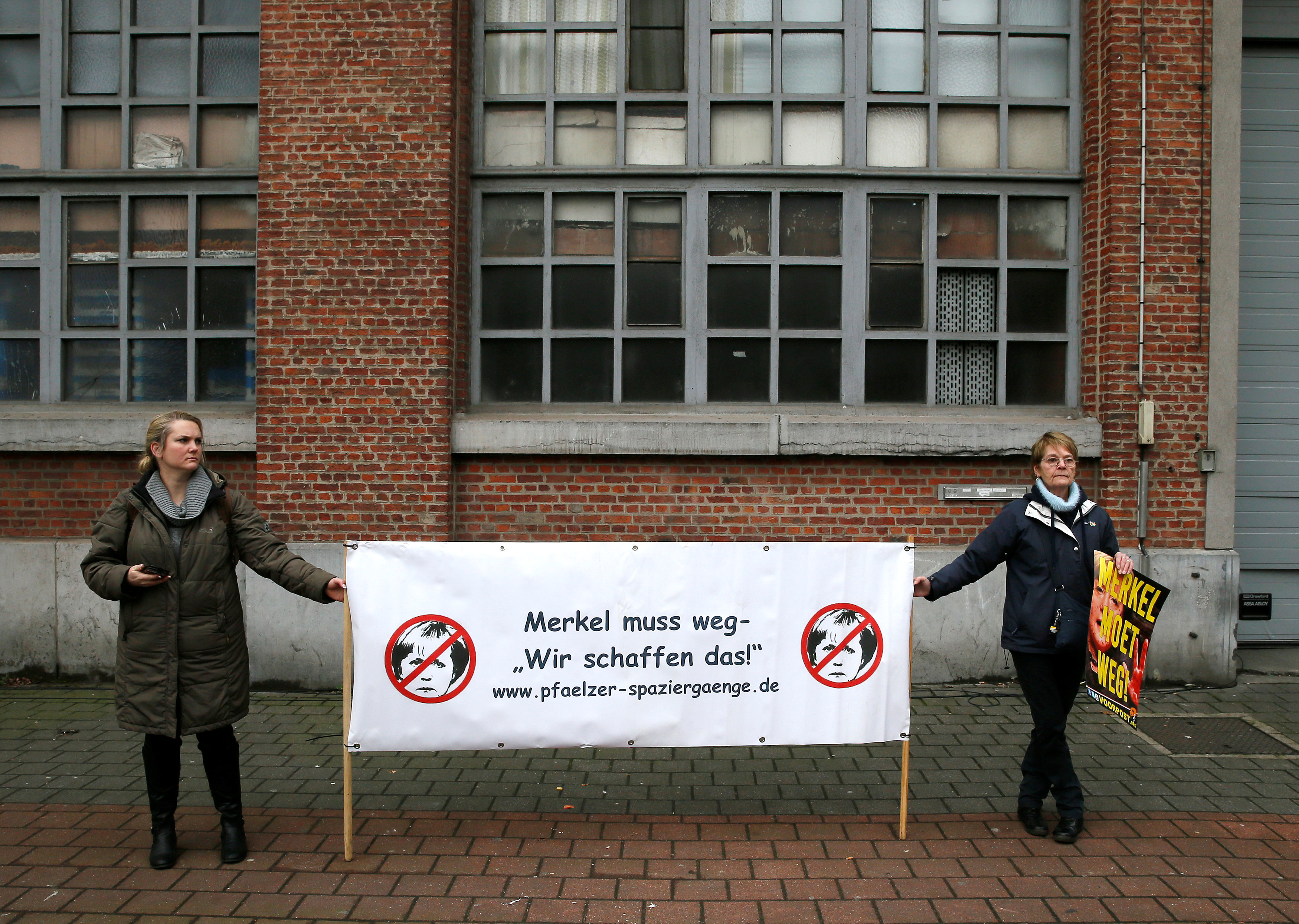 سيدتان تحملان لافتة مناهضة للمستشارة الألمانية انجيلا ميركل