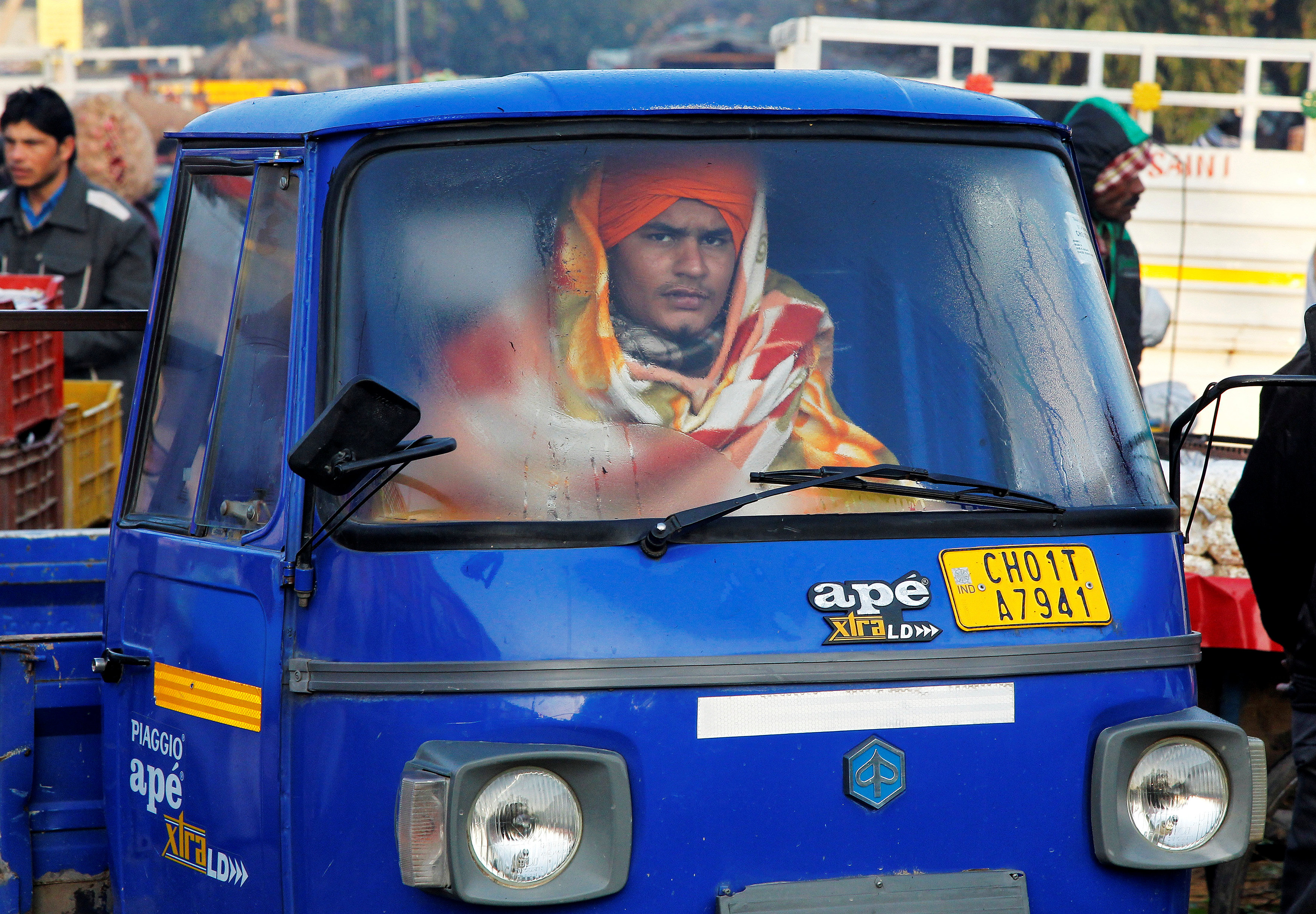 رجل يتعطى ببطانية أثناء قيادته سيارة فى سوق للجملة بالهند