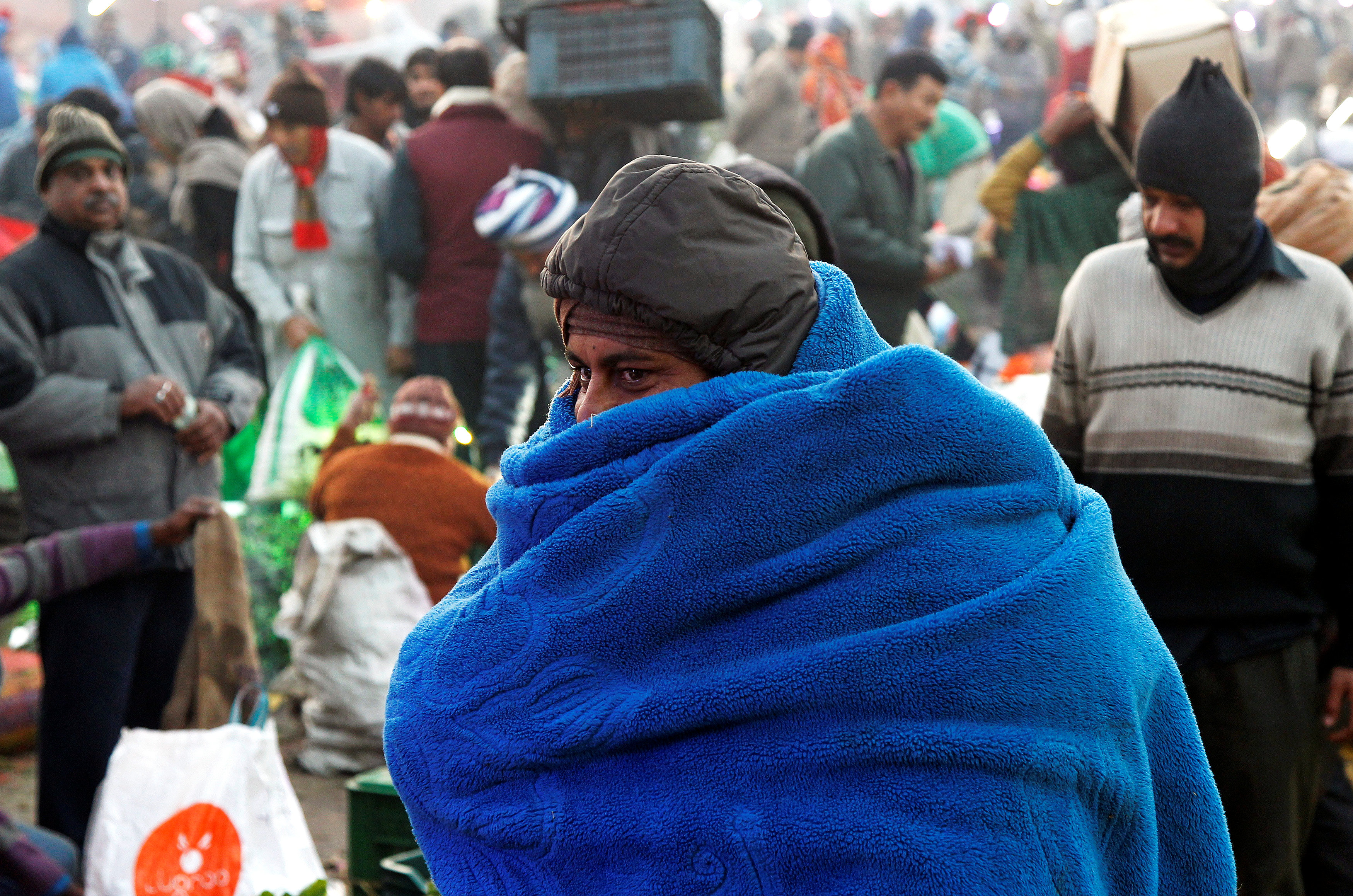 رجل يتغطى ببطانية فى سوق للجملة بالهند لسوء الأحوال الجوية