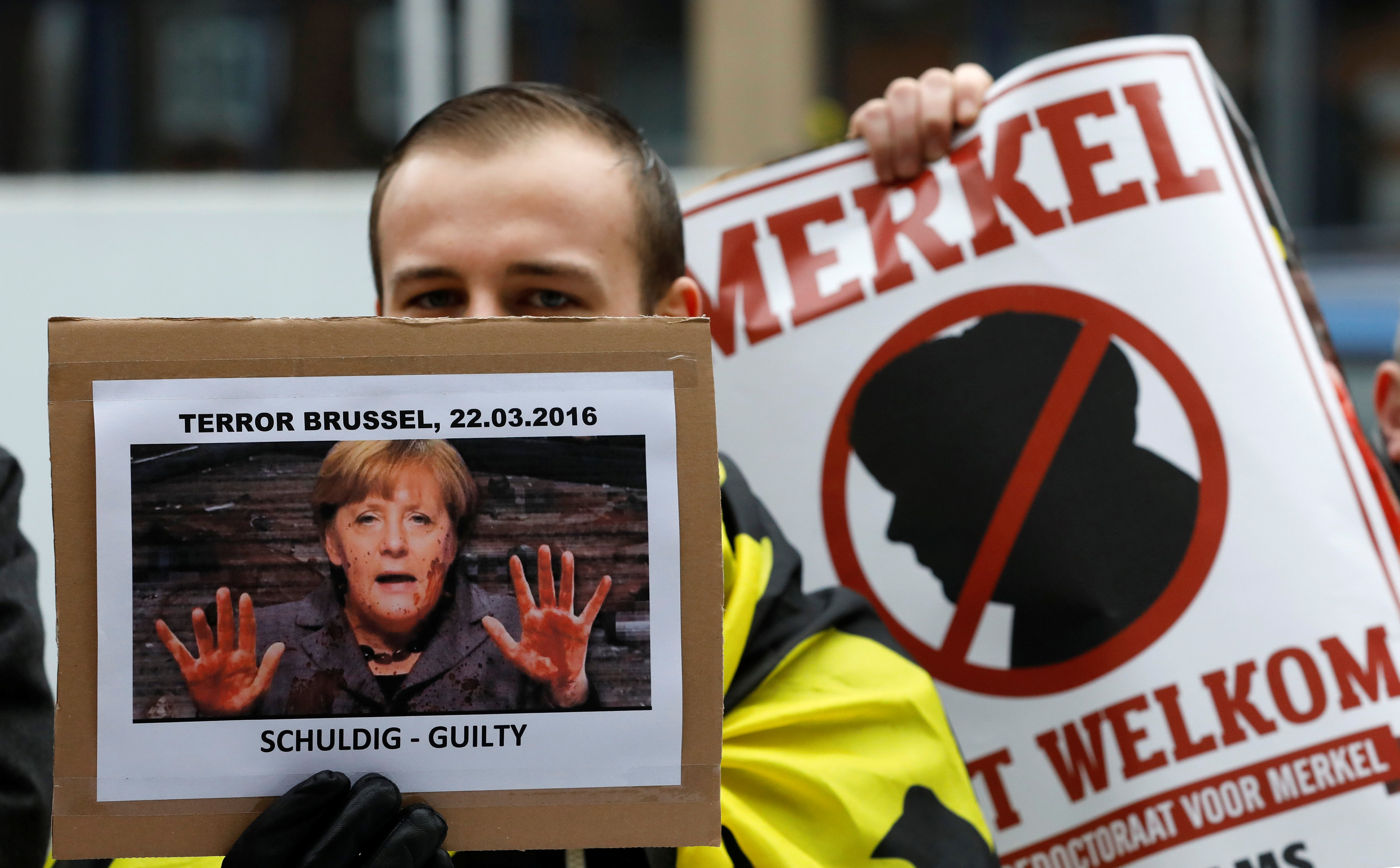 المتظاهرون يرفعون لافتات مناهضة للمستشارة الألمانية انجيلا ميركل