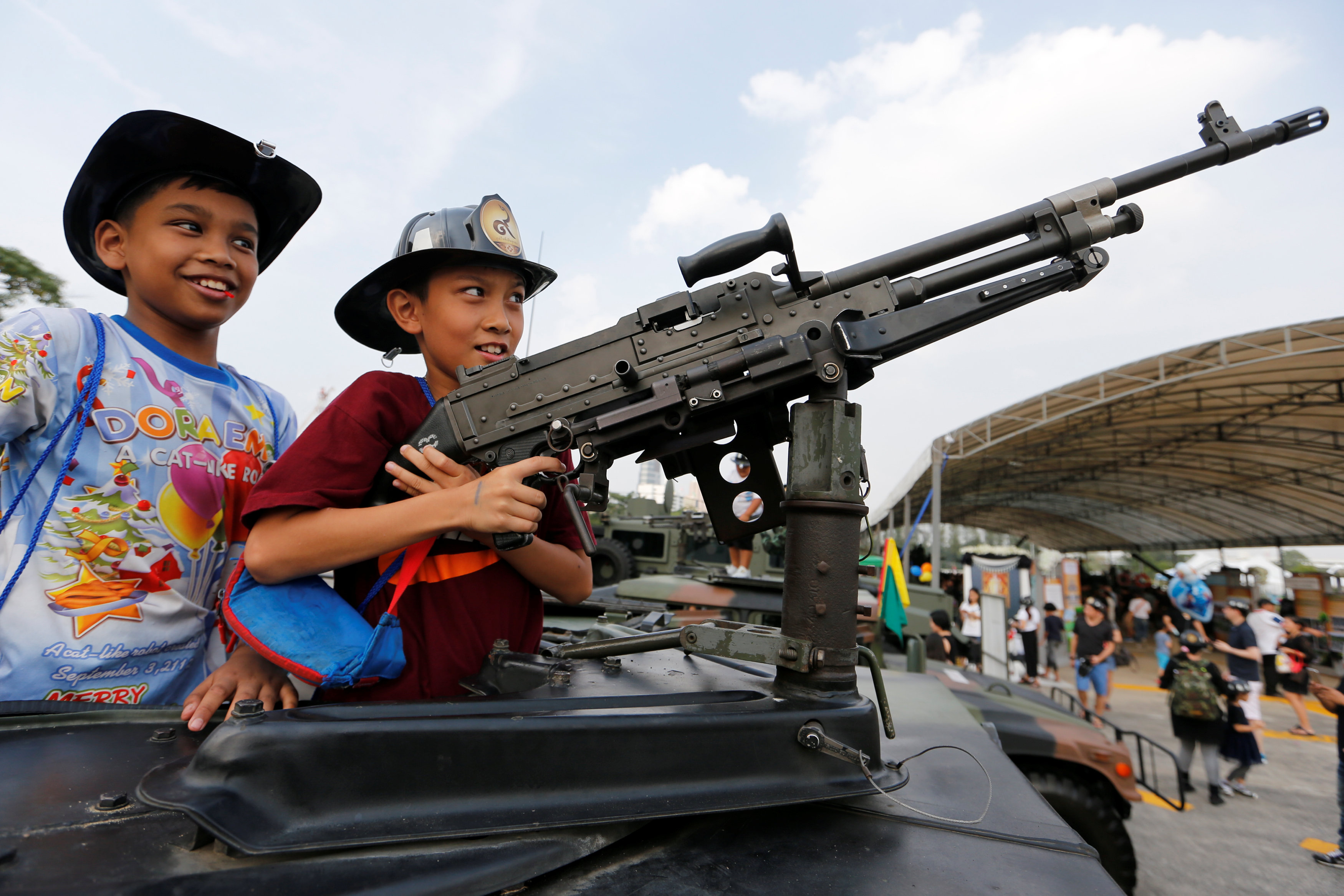 أطفال يمسكون بالسلاح أعلى سيارة مصفحة خلال احتفالات يوم الطفل فى تايلاند