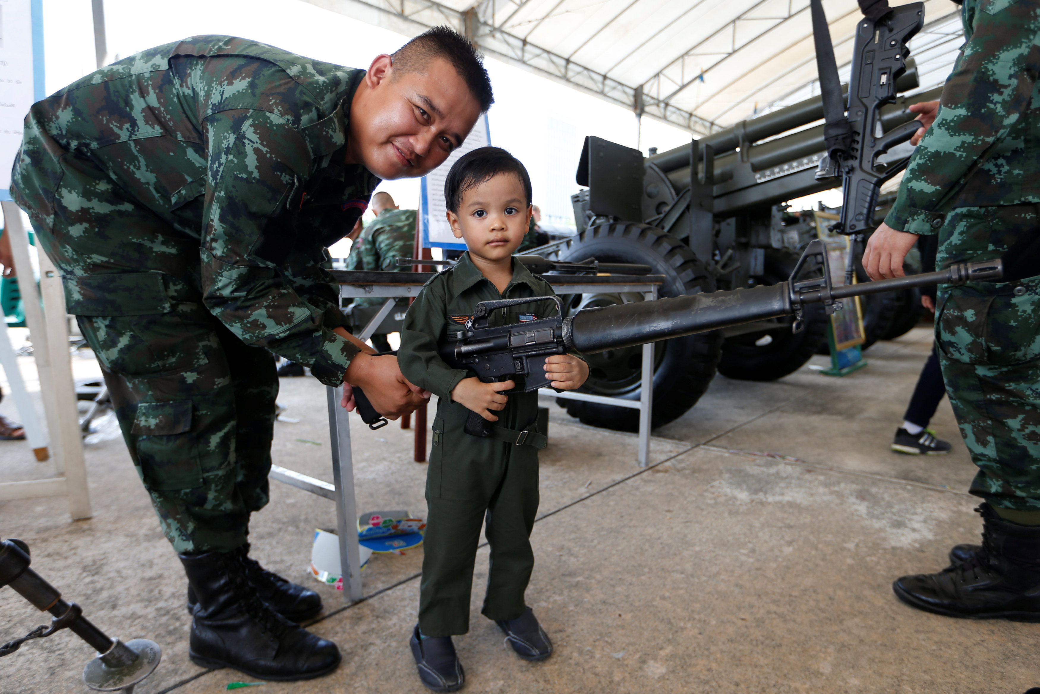 جندى يساعد طفل على الامساك بسلاح آلى فى احتفالات يوم الطفل بتايلاند