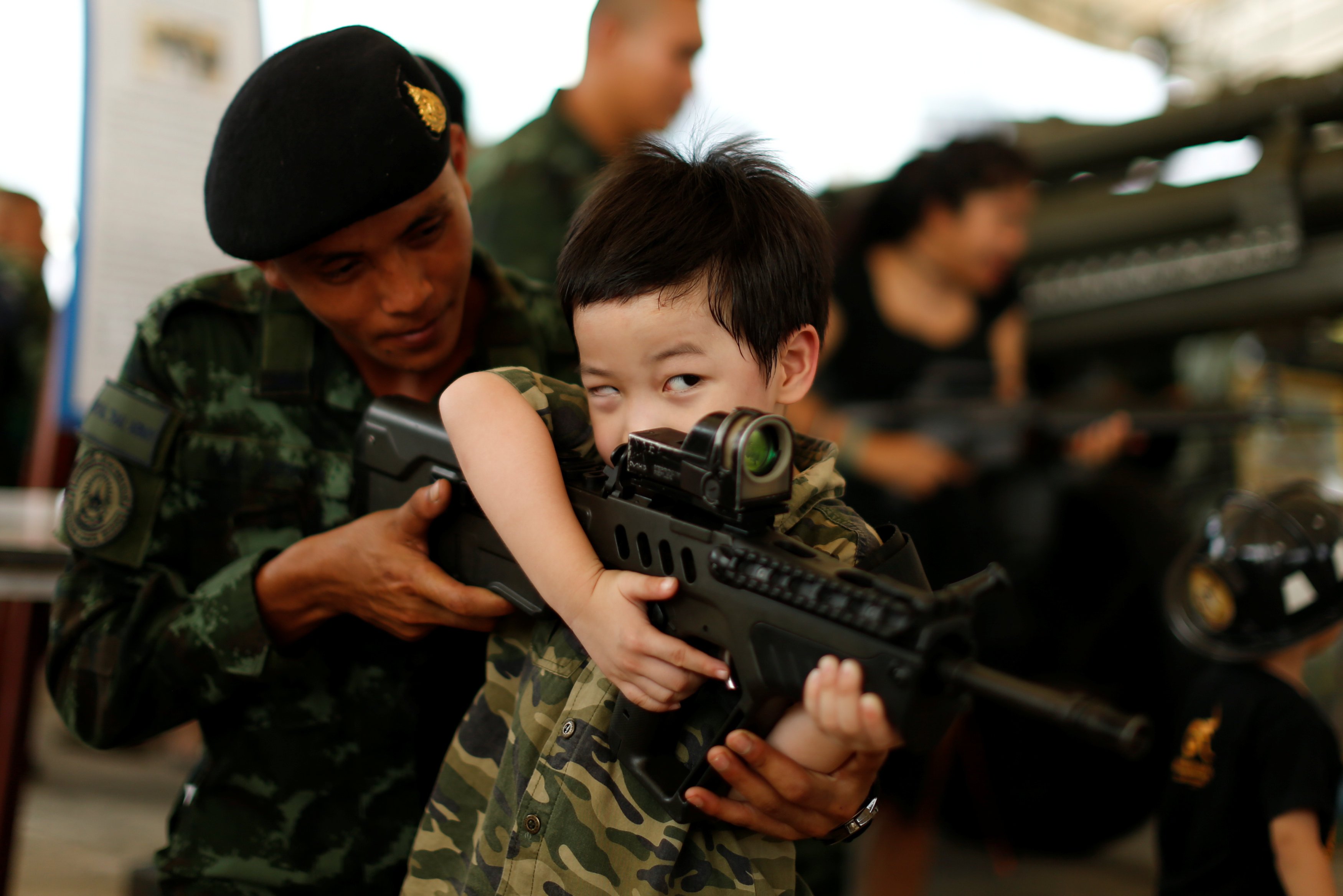 جندى يمسك بيد طفل ليحمل سلاح آلى فى احتفالات يوم الطفل بتايلاند