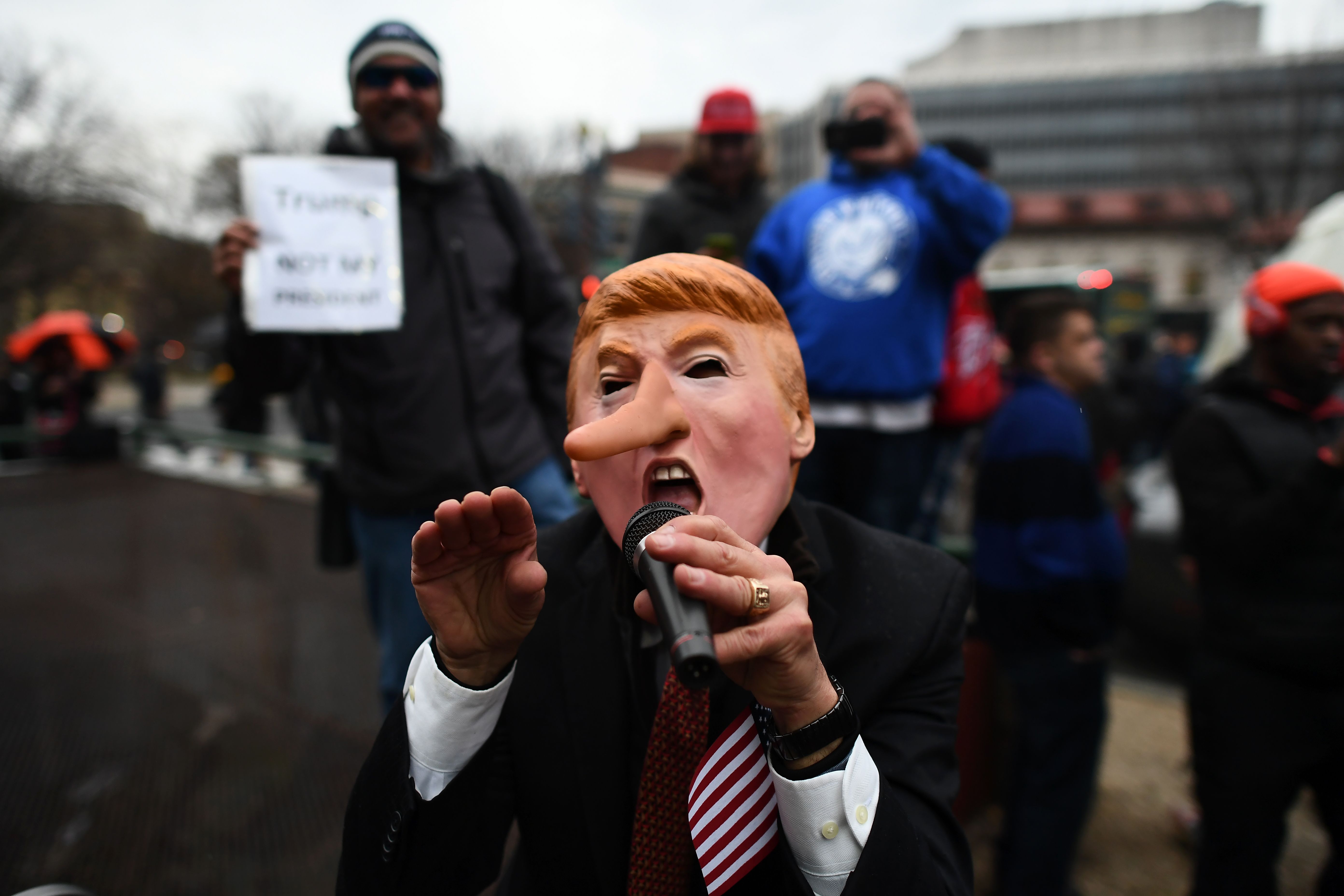 متظاهر يرتدى قناعًا ساخرًا من ترامب يتحدث فى مايكروفون لزملائه