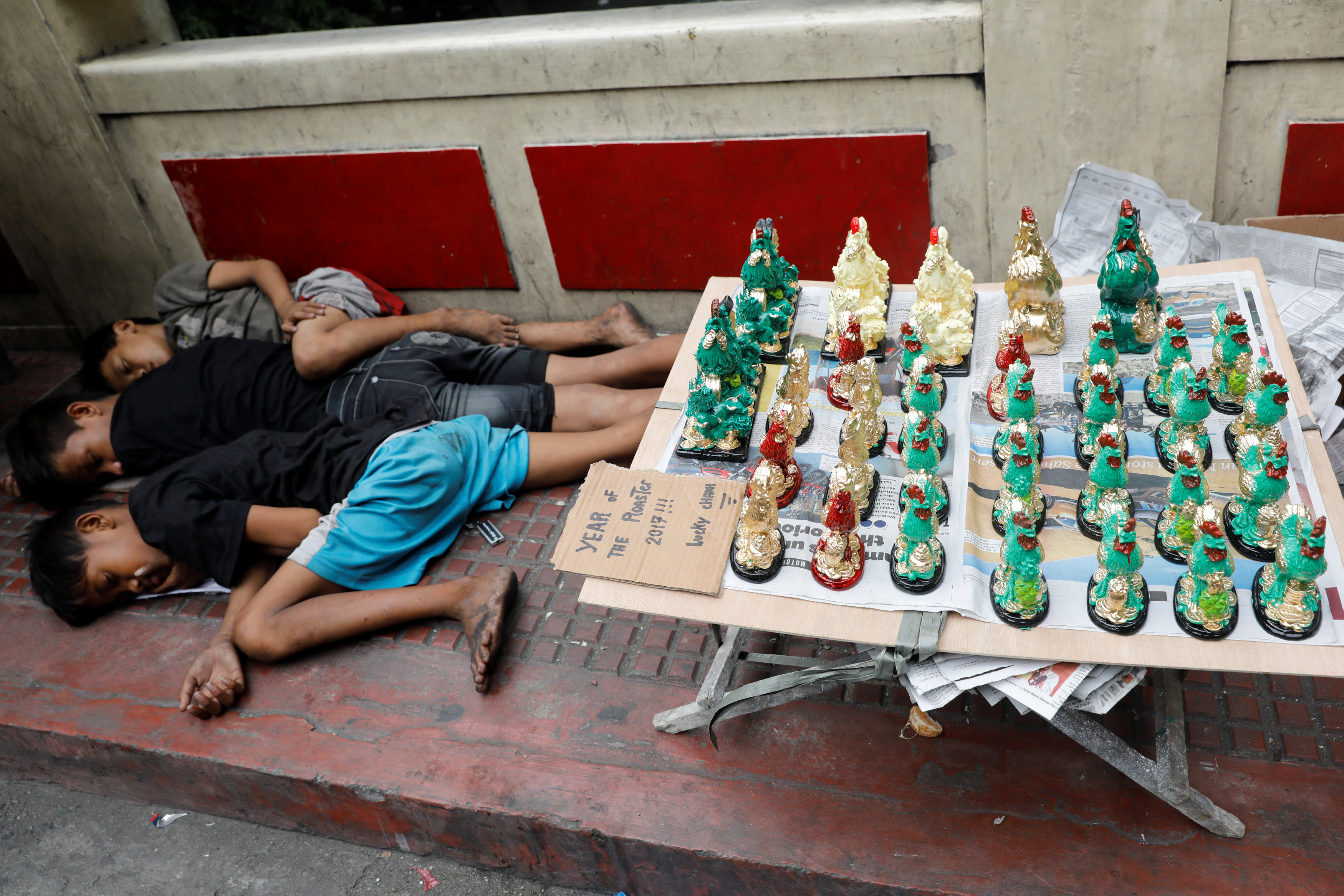 أطفال ينامون بجانب تماثيل الديك التى يبيعونها بمناسبة السنة الصينية الجديدة فى الفلبين