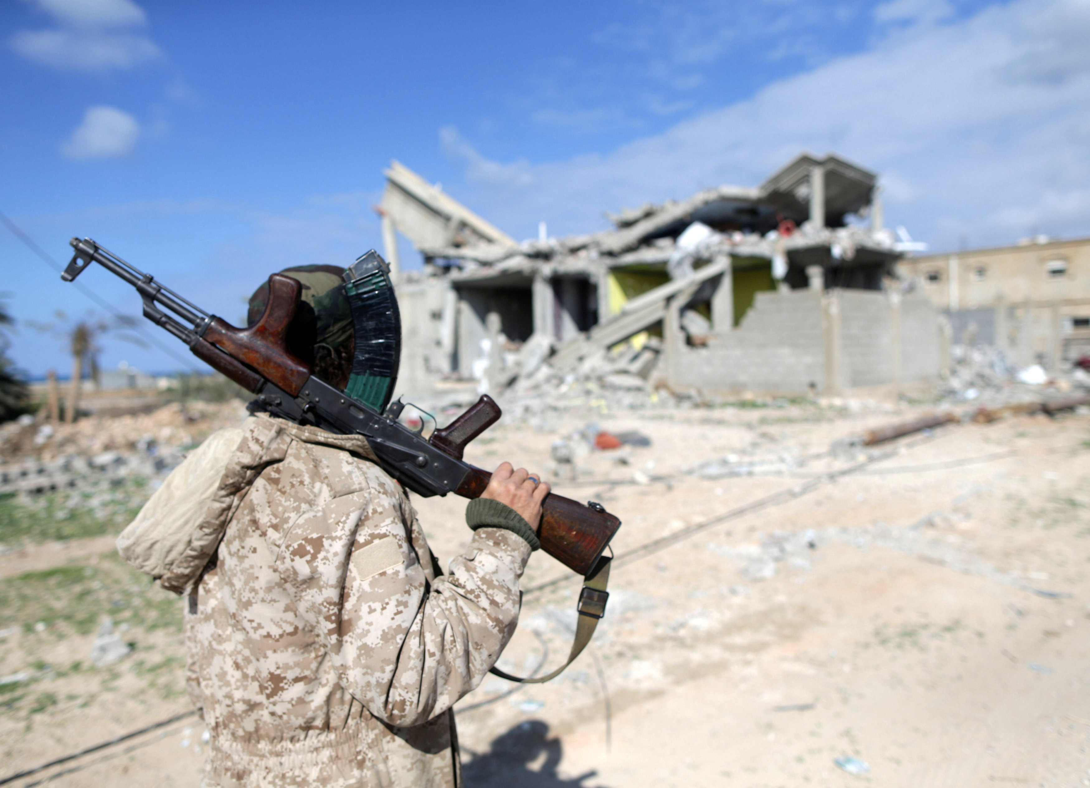  أحد أفراد القوات الليبية يقف أمام منزل مدمر