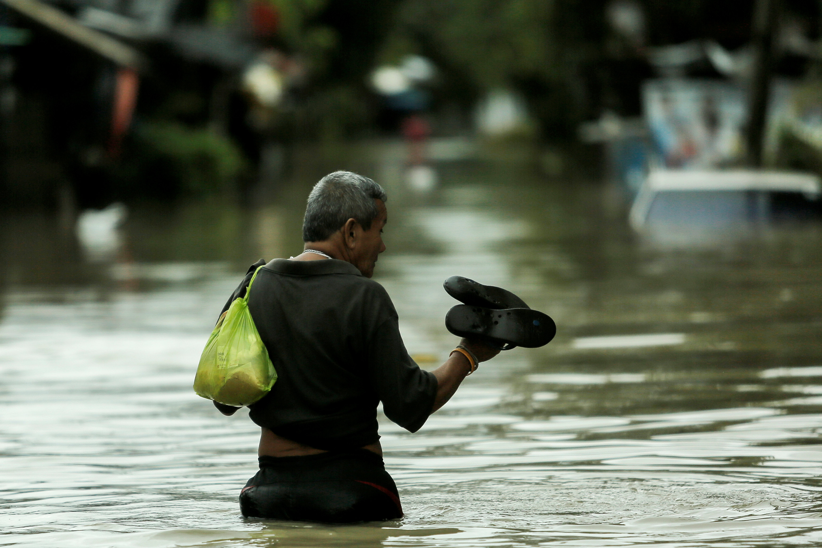 رجل يخلع حذائه ليسير فى مياه الفيضانات بسواع مقاطعة موانج - رويترز