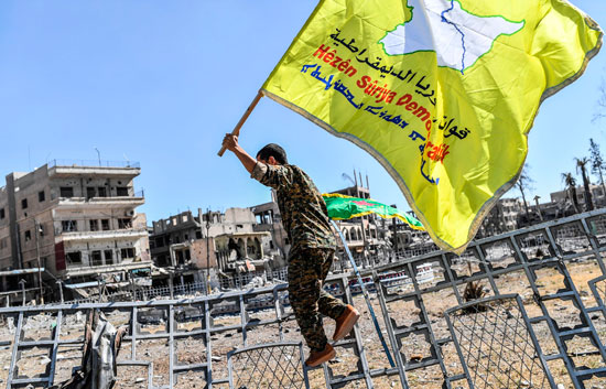 جندى يحمل علم سوريا الديمقراطية ابتهاجًا بالانتصار على داعش