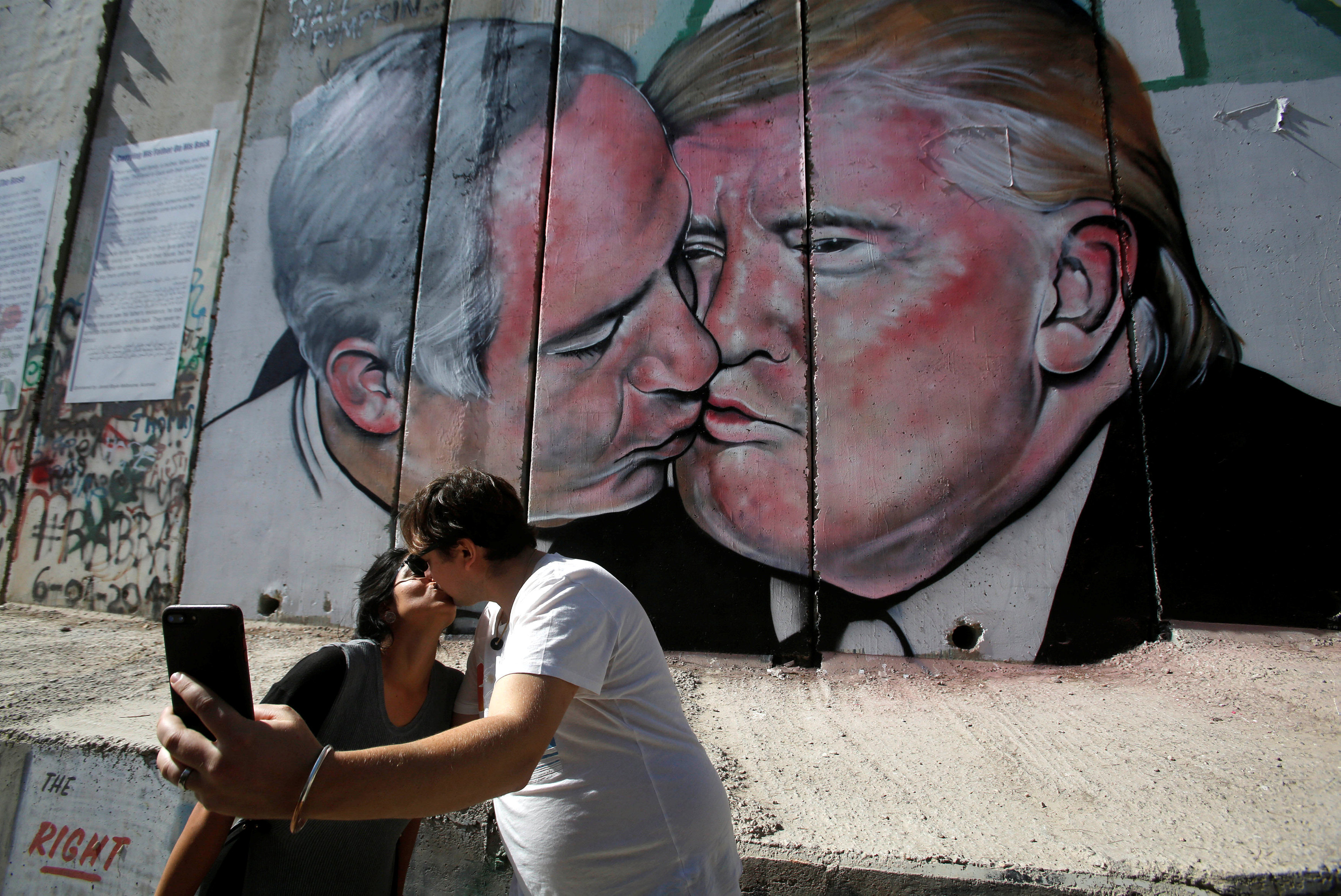 رجل وزوجته يلتقطان صورة سيلفى مع جرافيتى ترامب ونتنياهو