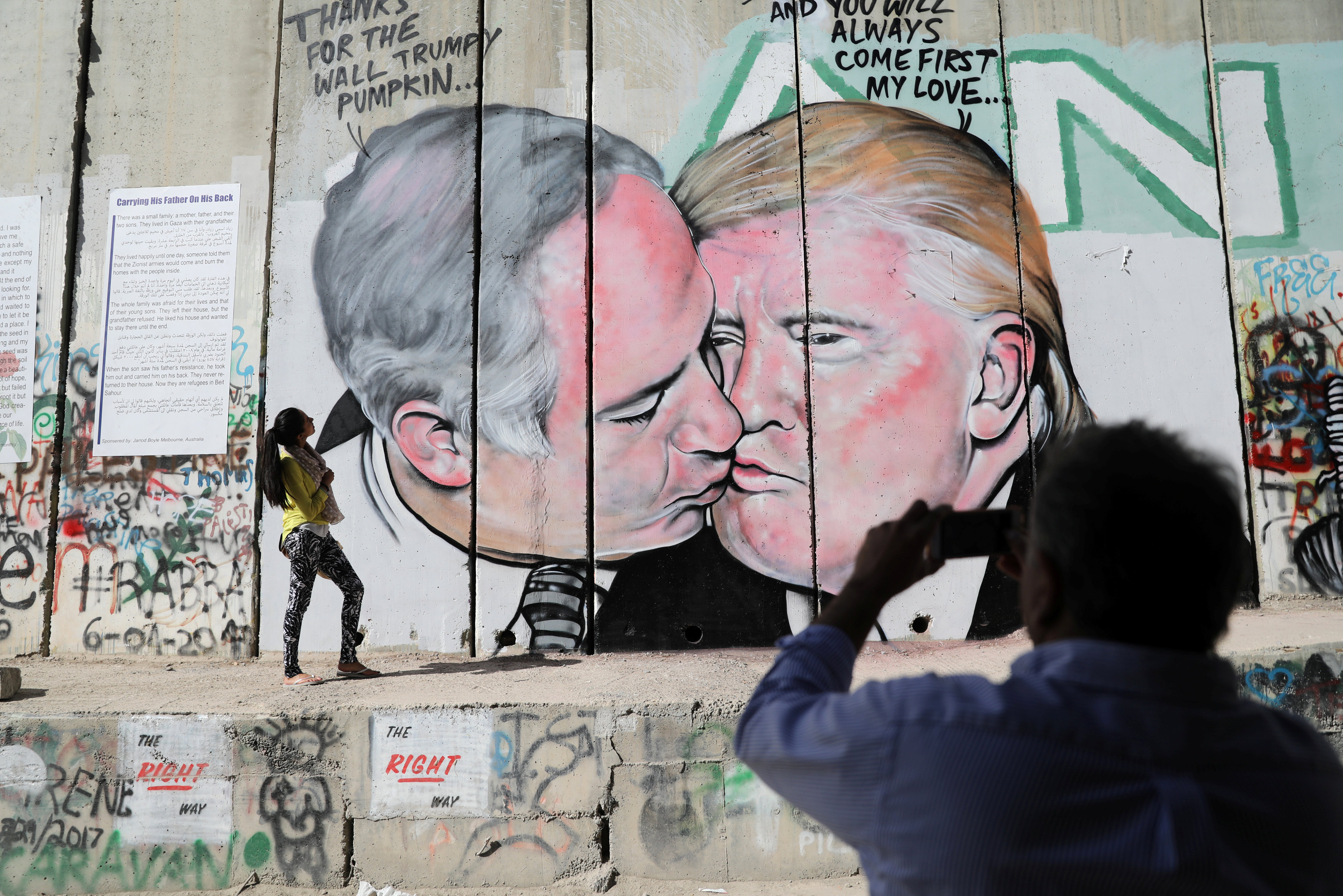 رجل يلتقط صورة لفتاة أمام جرافيتى ساخر من ترامب ونتنياهو