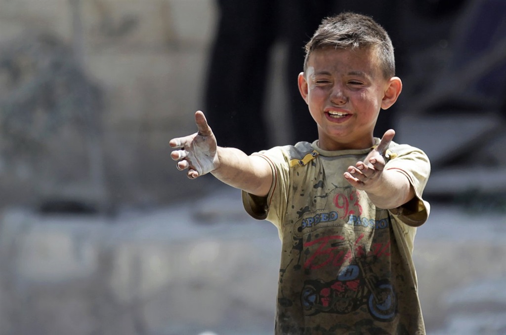 طفل يضحك رغم أثار تراب ركام القصف على وجهه