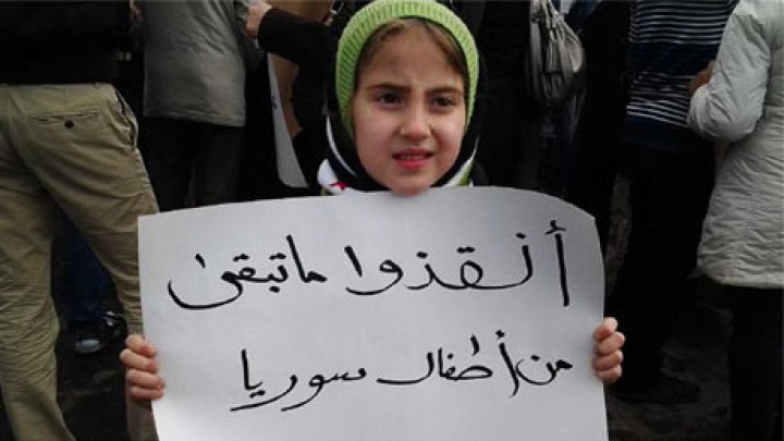 طفلة تحمل لافتة مكتوب عليها "أنقذوا أطفال سوريا"