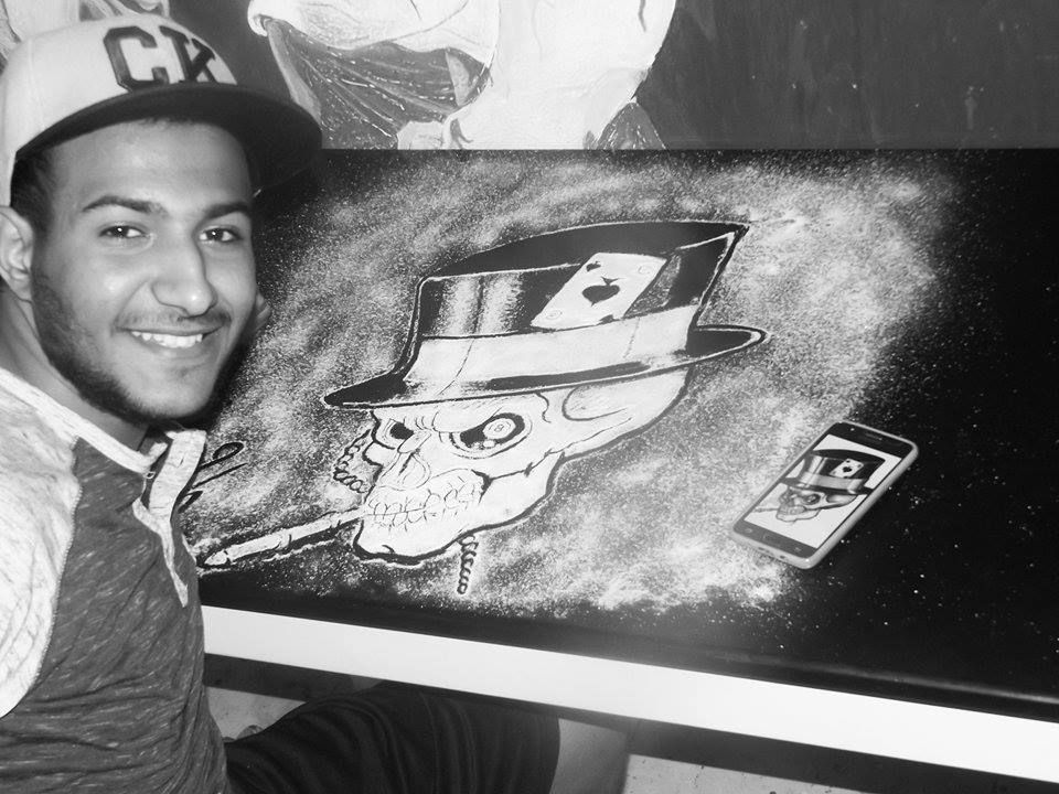 الشاب حسن محمد مع إحدى رسوماته الإبداعية بالملح