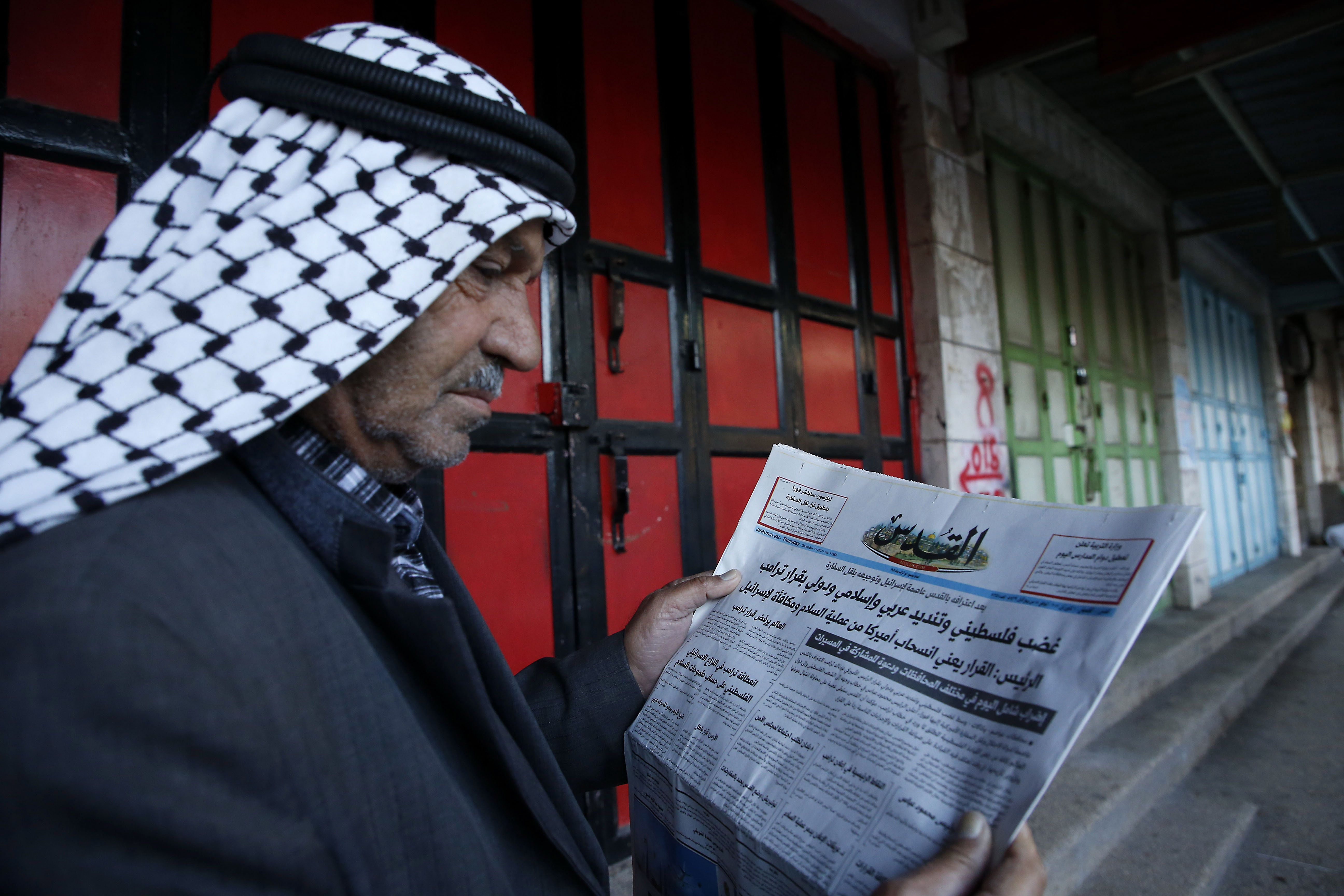 رجل فلسطينى يجلس أمام محله المغلق ويقرأ الجرايد