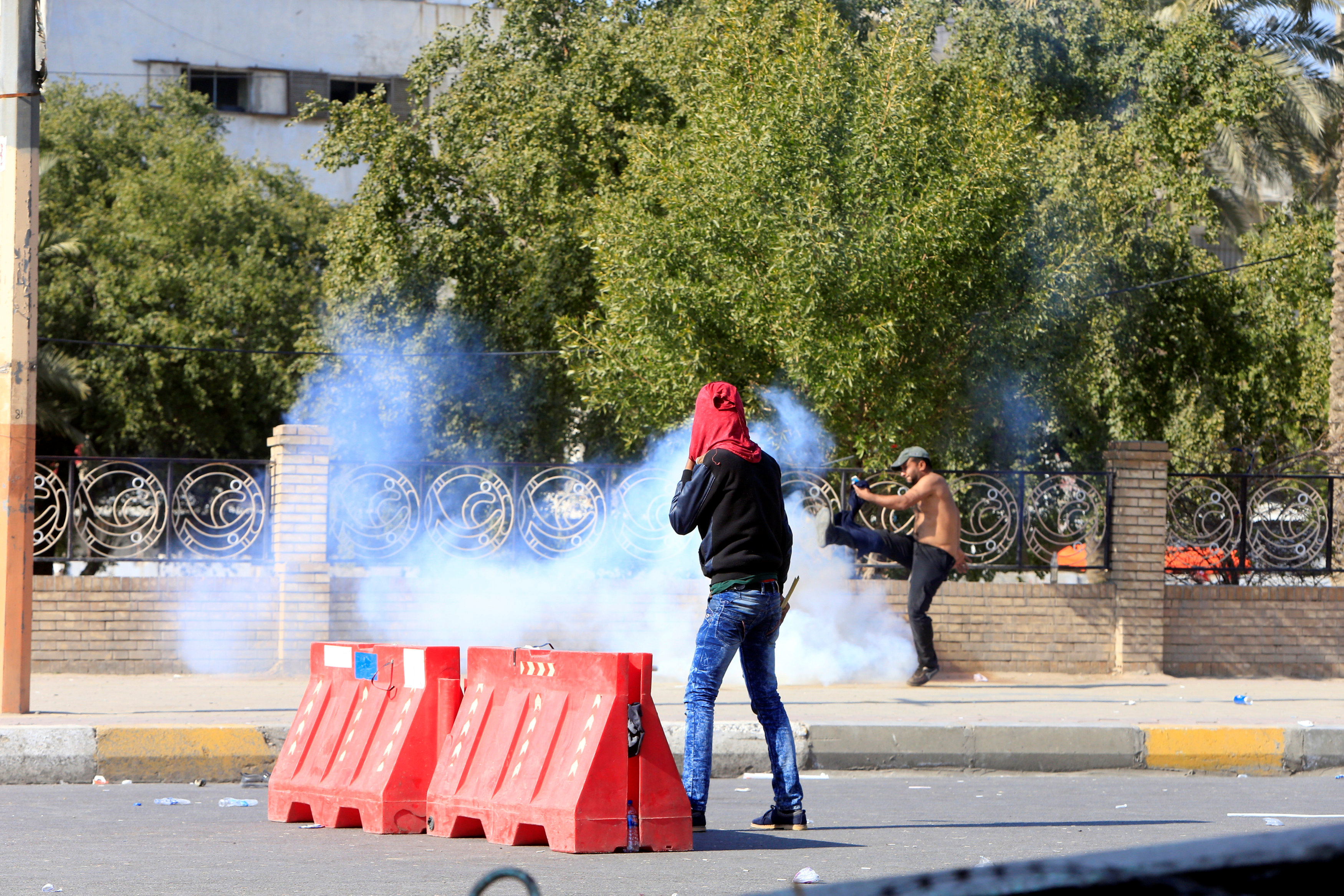 متظاهر عراقى يركل قنبلة الغاز بقدمه لإبعادها عنه
