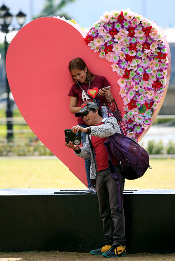 رجل وزوجته يلتقطان صورة سيلفى وخلفها قلب احتفالًا بعيد الحب