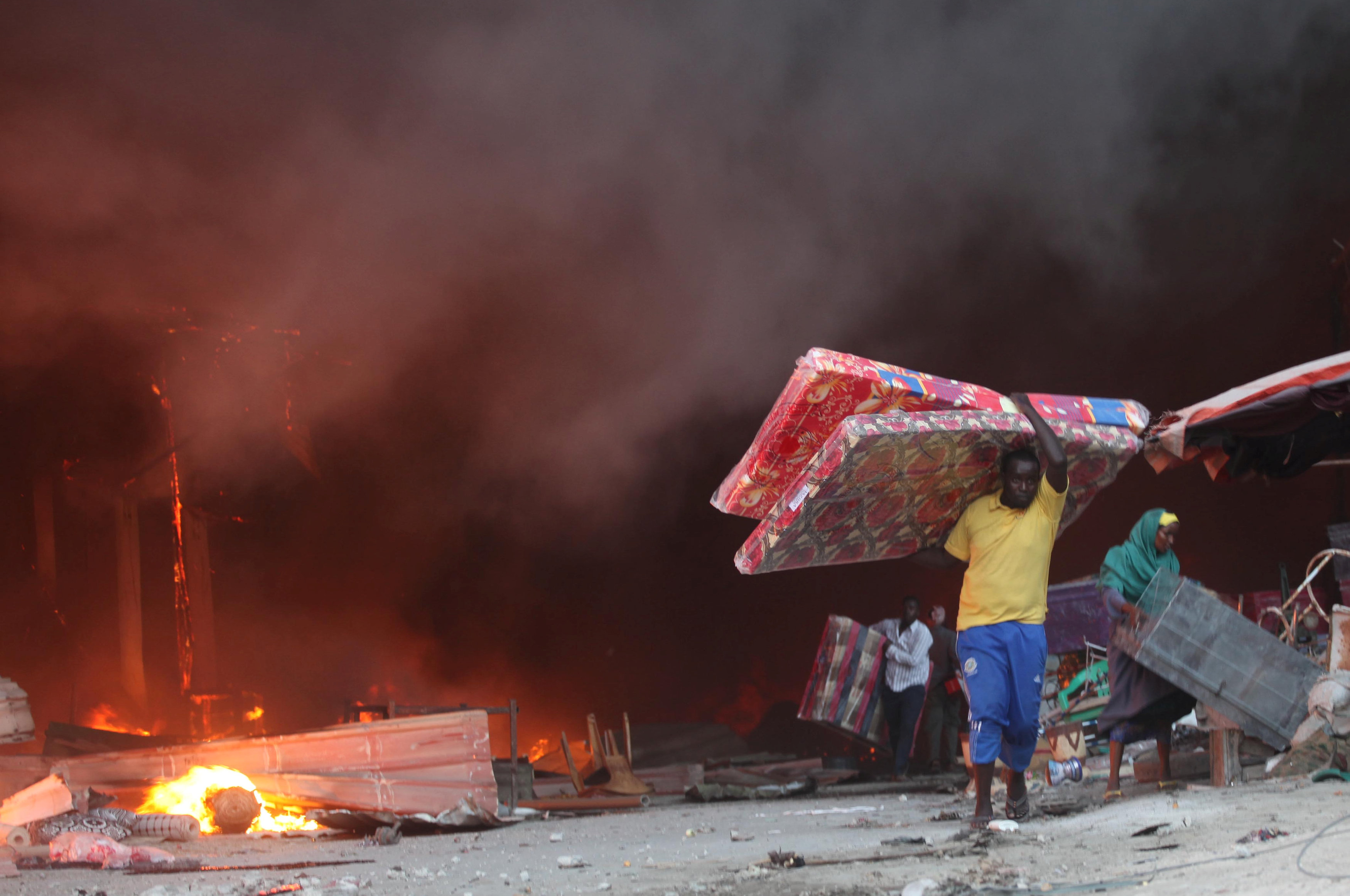 مواطنون يحملون مراتب للنوم ويخرجون من وسط الدخان المتصاعد بالسوق المحترق فى الصومال