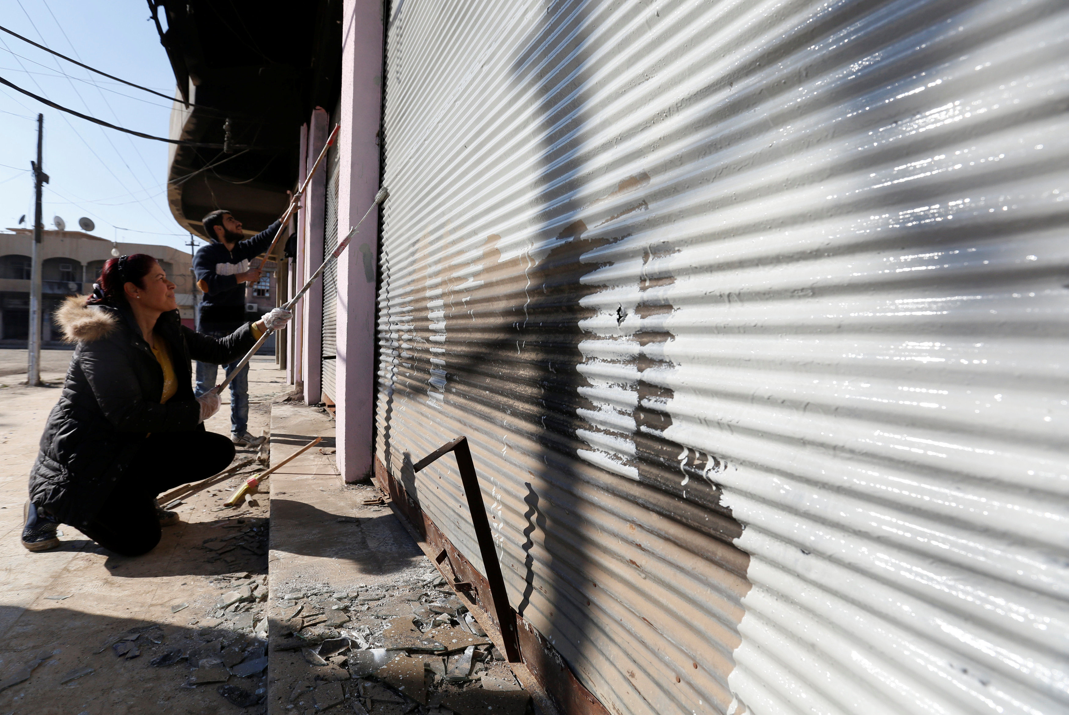 مواطنون عراقيين يقومون بطلاء واجهات المحلات لإزالة أثار عبارات داعش الإرهابية