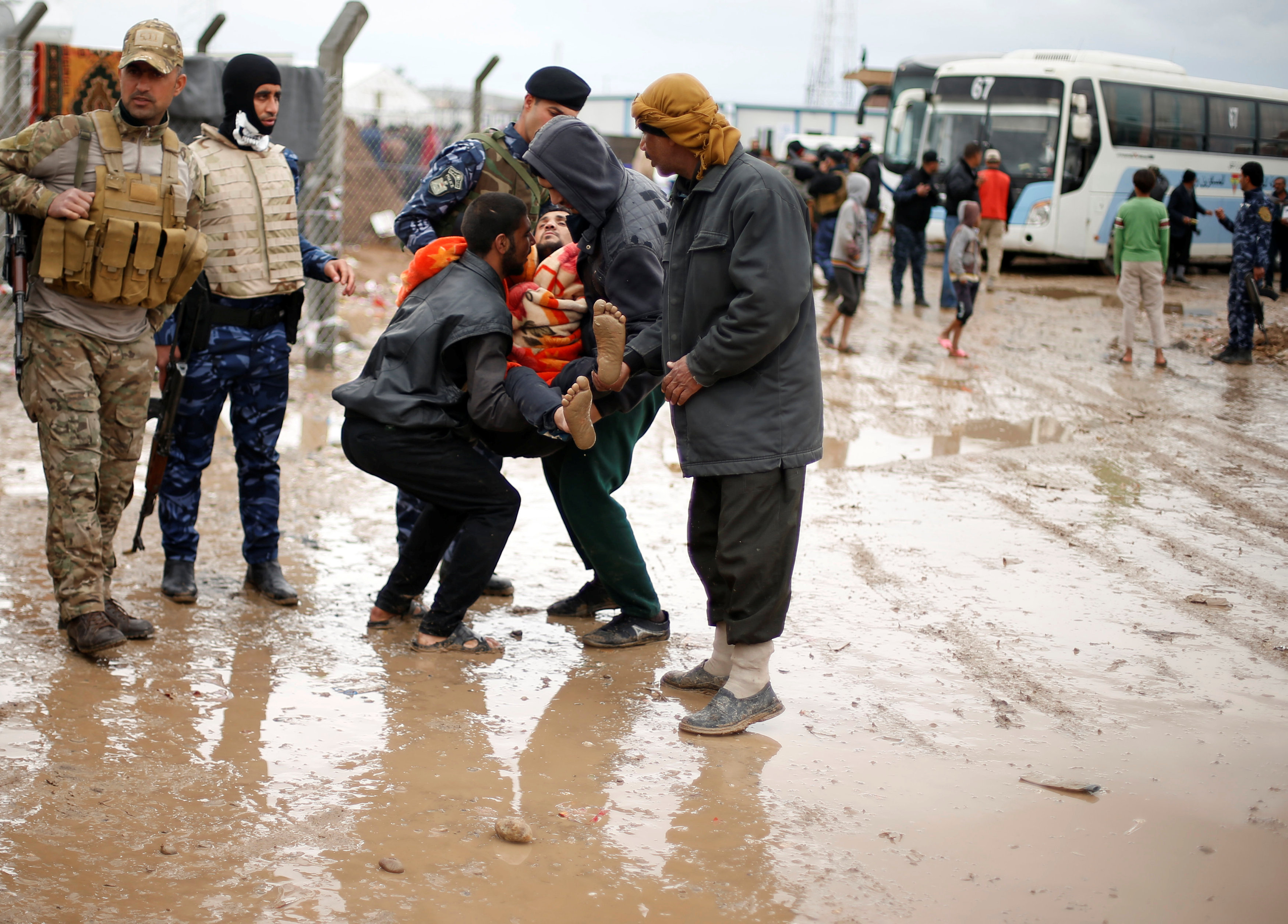 نازحون يحملون عراقيا خلال توجههم للمخيمات وسط المطر