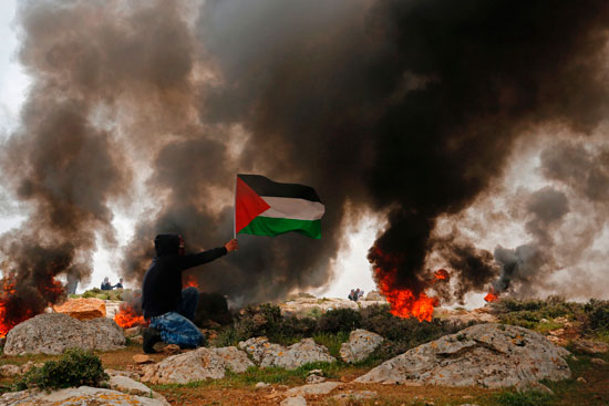 شاب فلسطينى يرفع علم بلاده خلال اشتباكات مع قوات الاحتلال فى رام الله