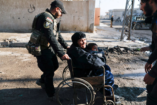 ضابط عراقى يجر كرسى متحركا لمساعدة سيدة مسنة