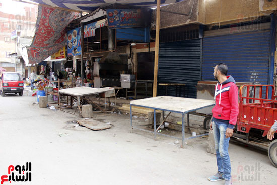 بائع يقف أمام  محله المغلق وشارع السوق بلا مشترين 