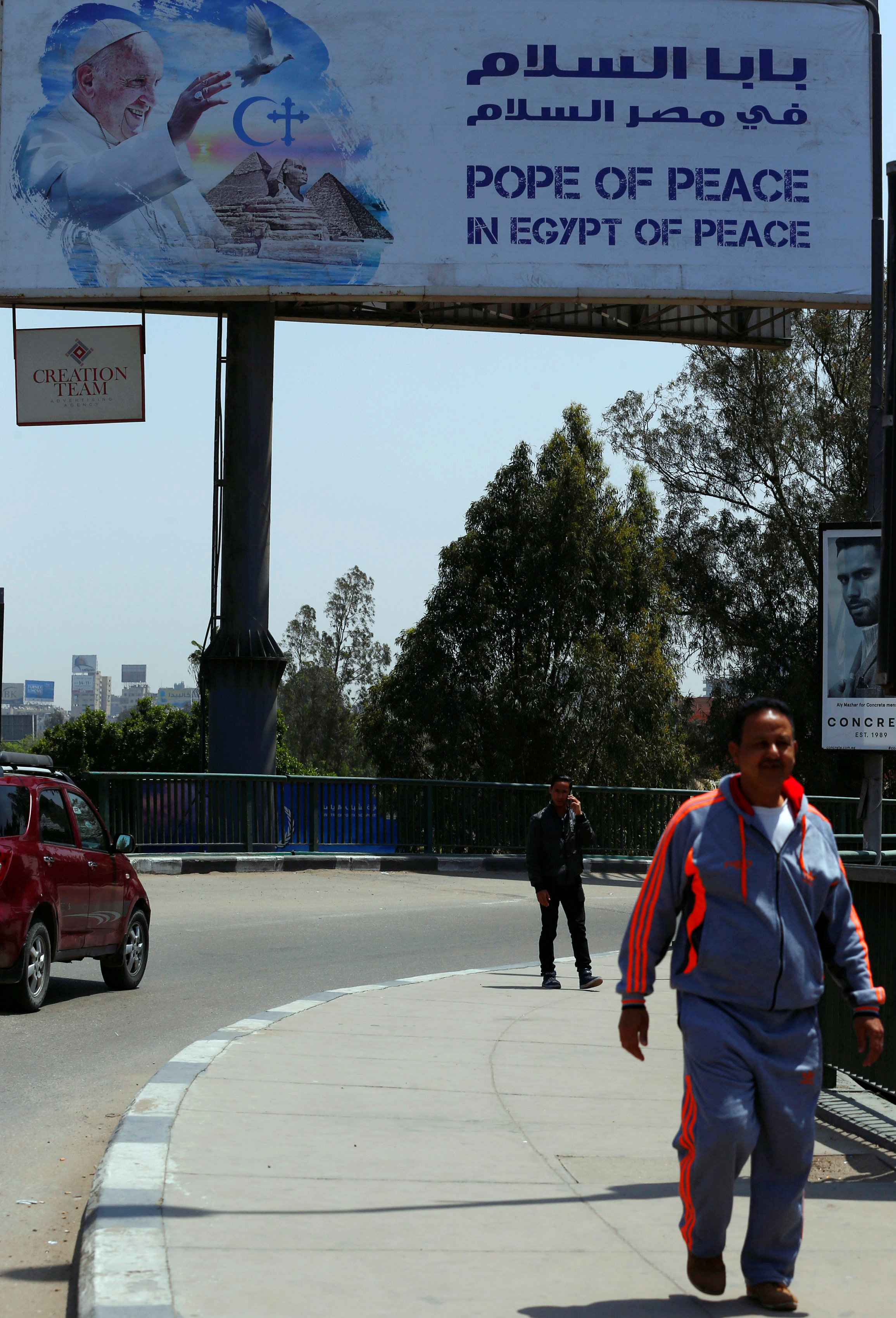 مواطنون يسيرون بالقرب من لوحة إعلانية عن بابا الفاتيكان