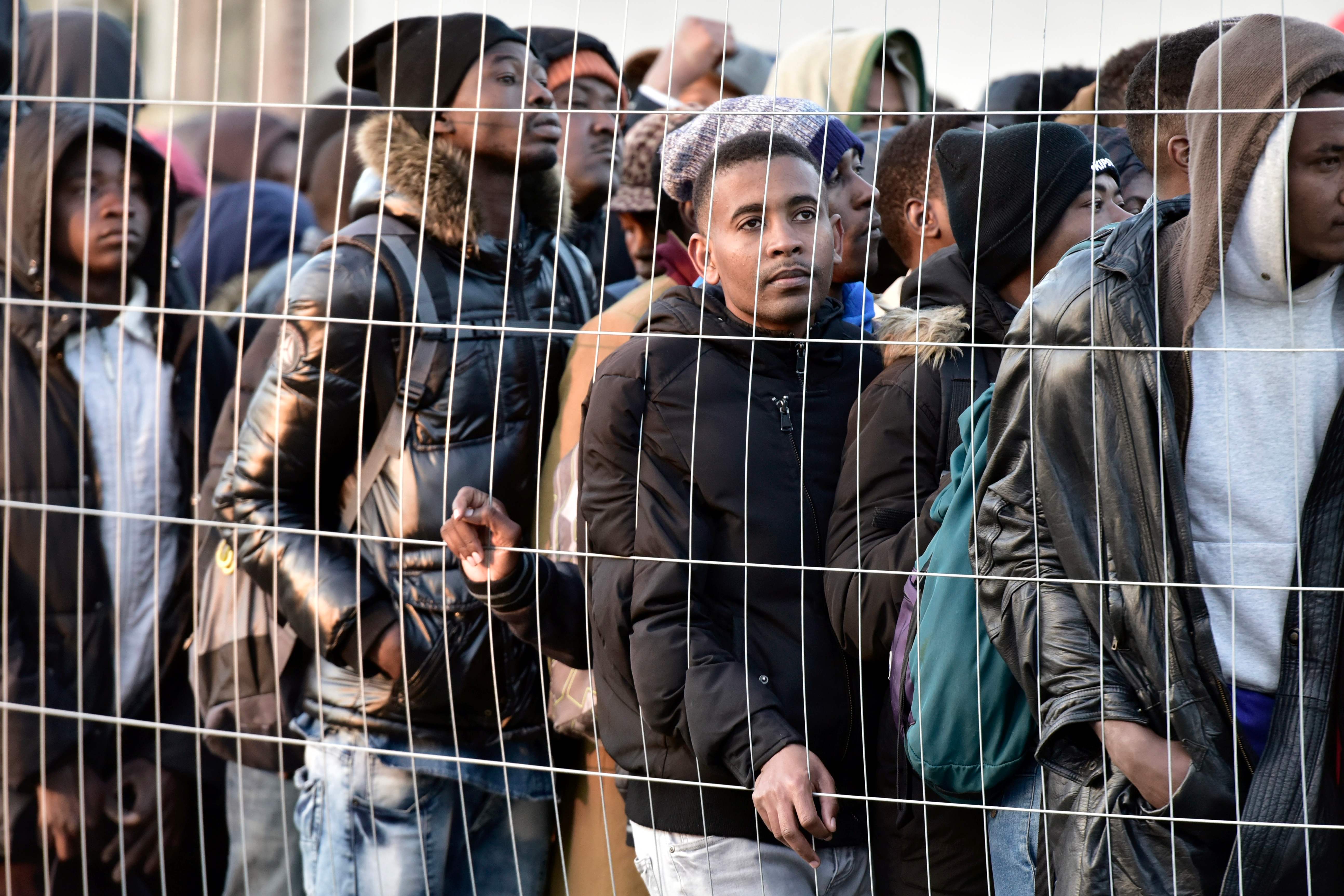 اللاجئين يقفون خلف أسلاك المخيم عقب اخلاؤه