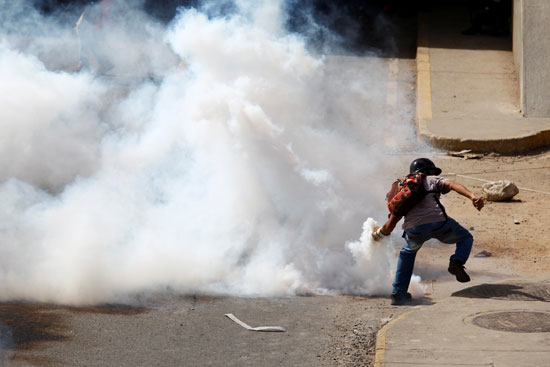 أحد المتظاهرين يلقى قنبلة غاز مسيل للدموع على قوات الأمن