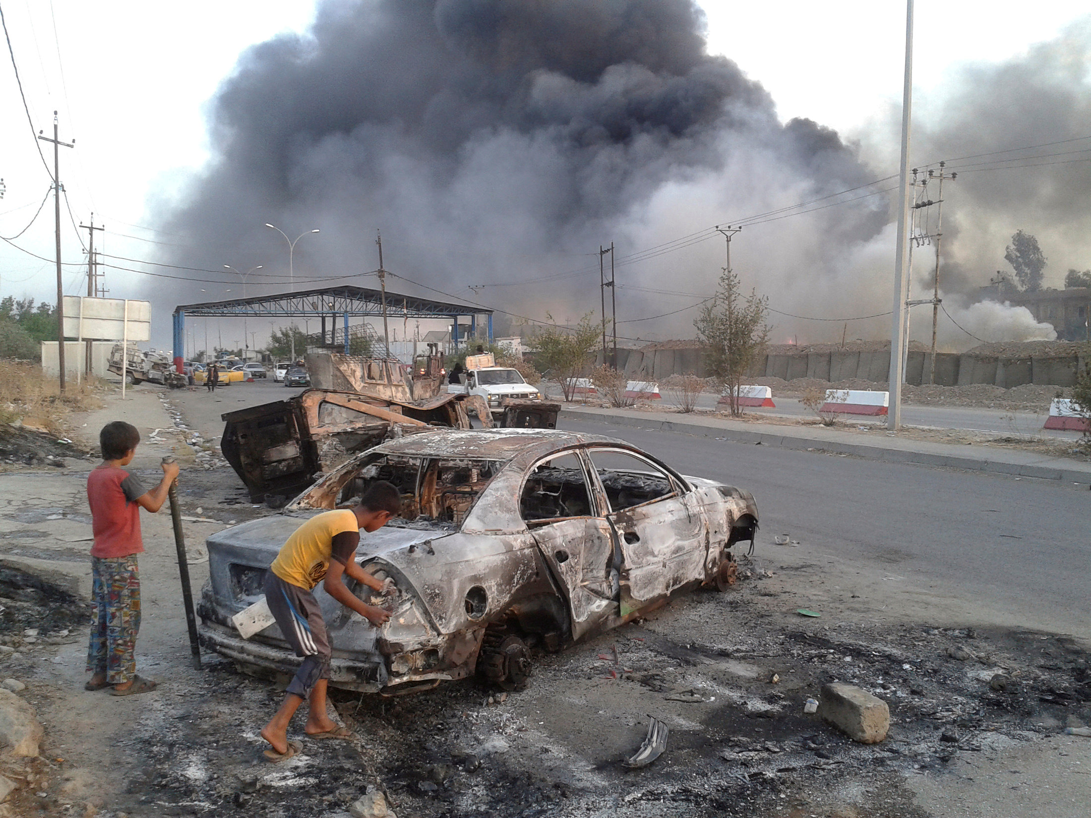 أطفال عراقيون يقفون بجوار سيارة متفحمة