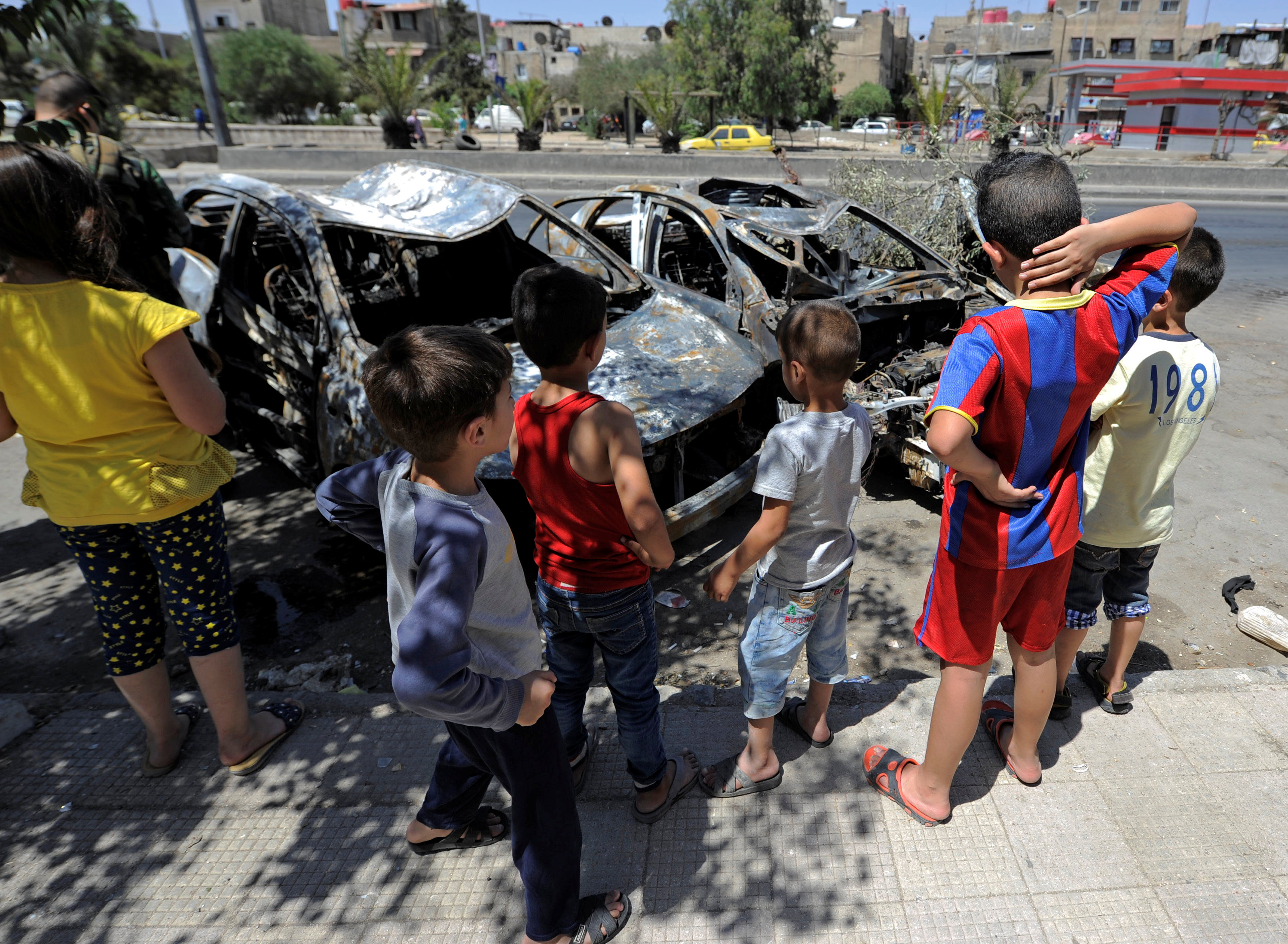 أطفال سوريون يقفون أمام سيارات متفحمة جراء القصف