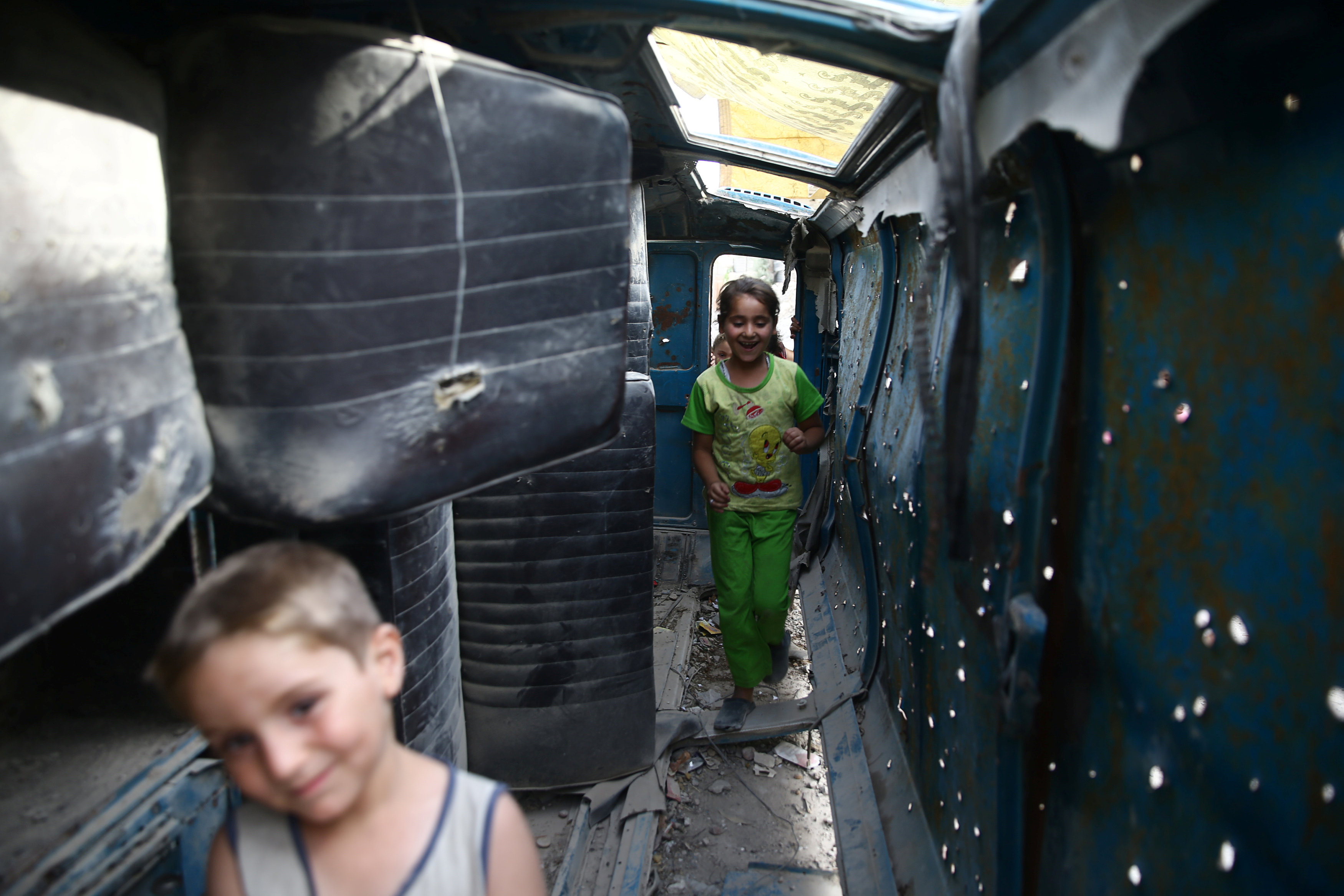 أطفال سوريون يلعبون داخل سيارة دمرت خلال الحرب