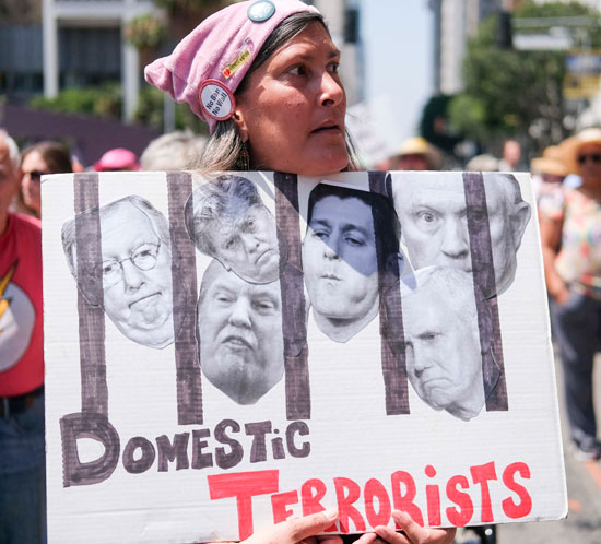 سيدة ترفع صورة تجمع المسئولين الأمريكيين خلف القضبان بينهم ترامب