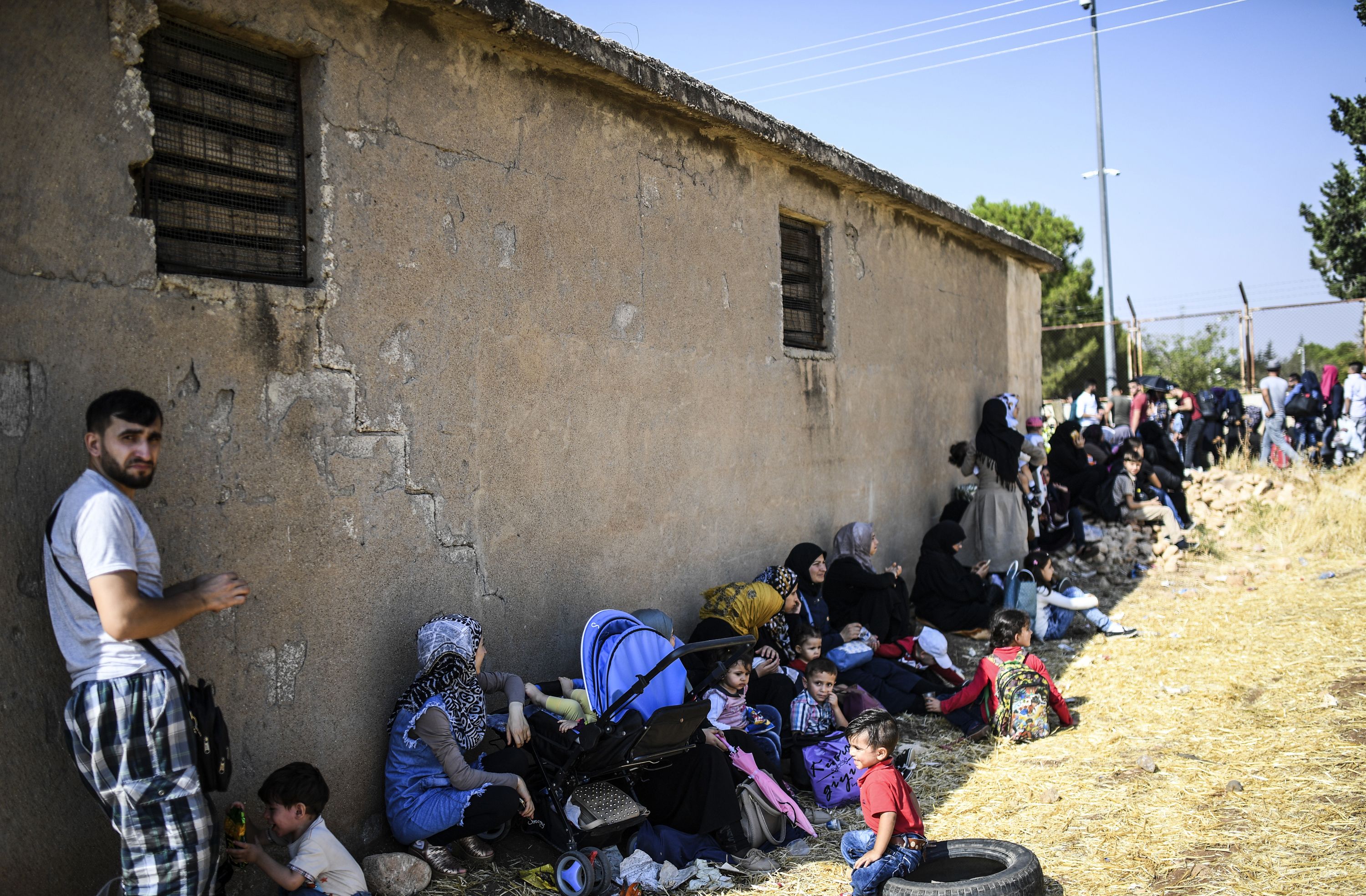 أسر سورية يحتمون بظل مبنى من حرارة الشمس على الحدود التركية