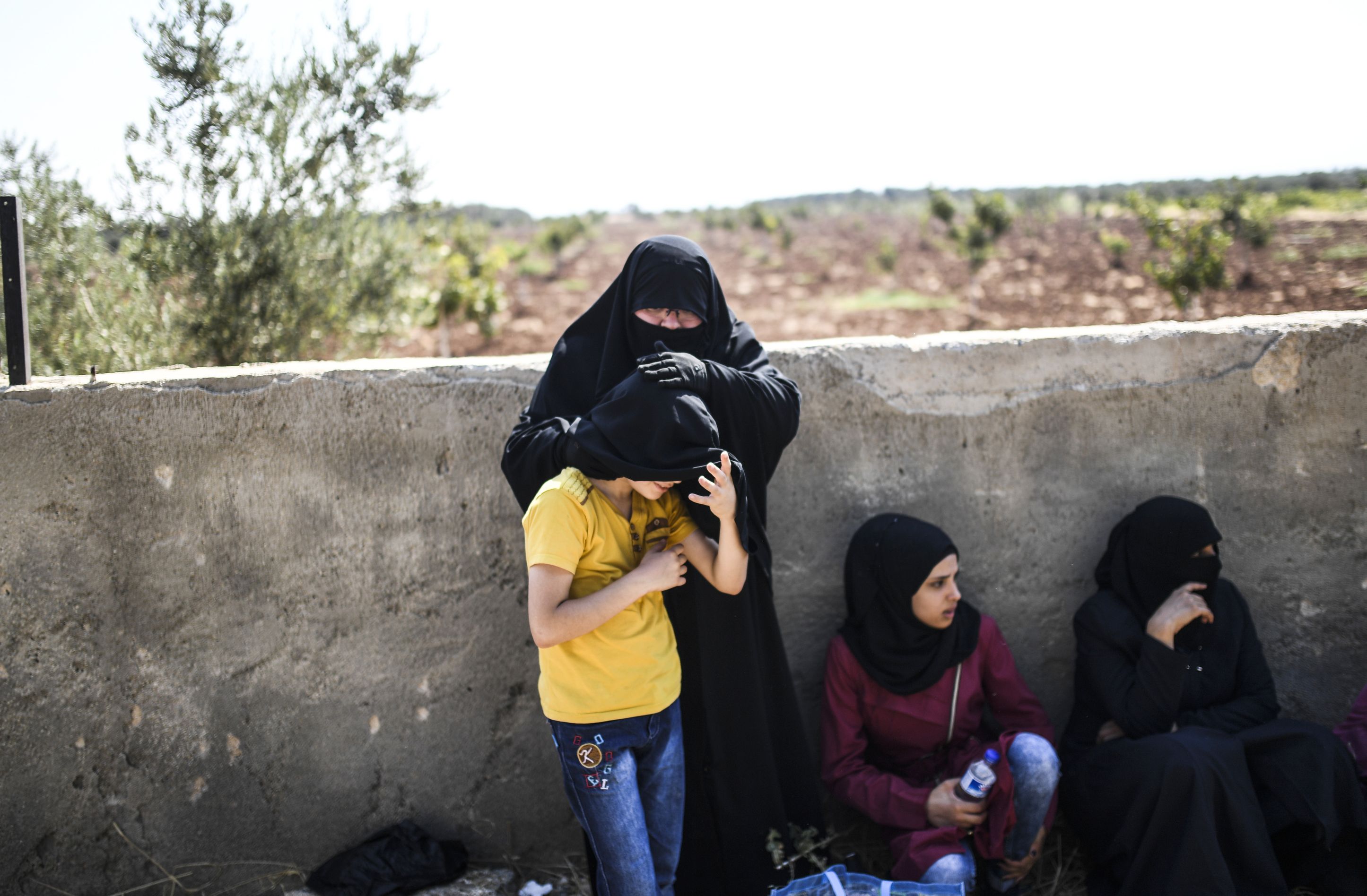 سيدة تحمى طفلها من حرارة الشمس على الحدود التركية السورية
