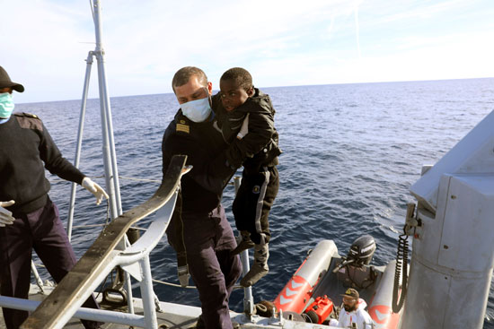 عسكرى ليبى يحمل طفل ضمن المهاجرين عبر البحر