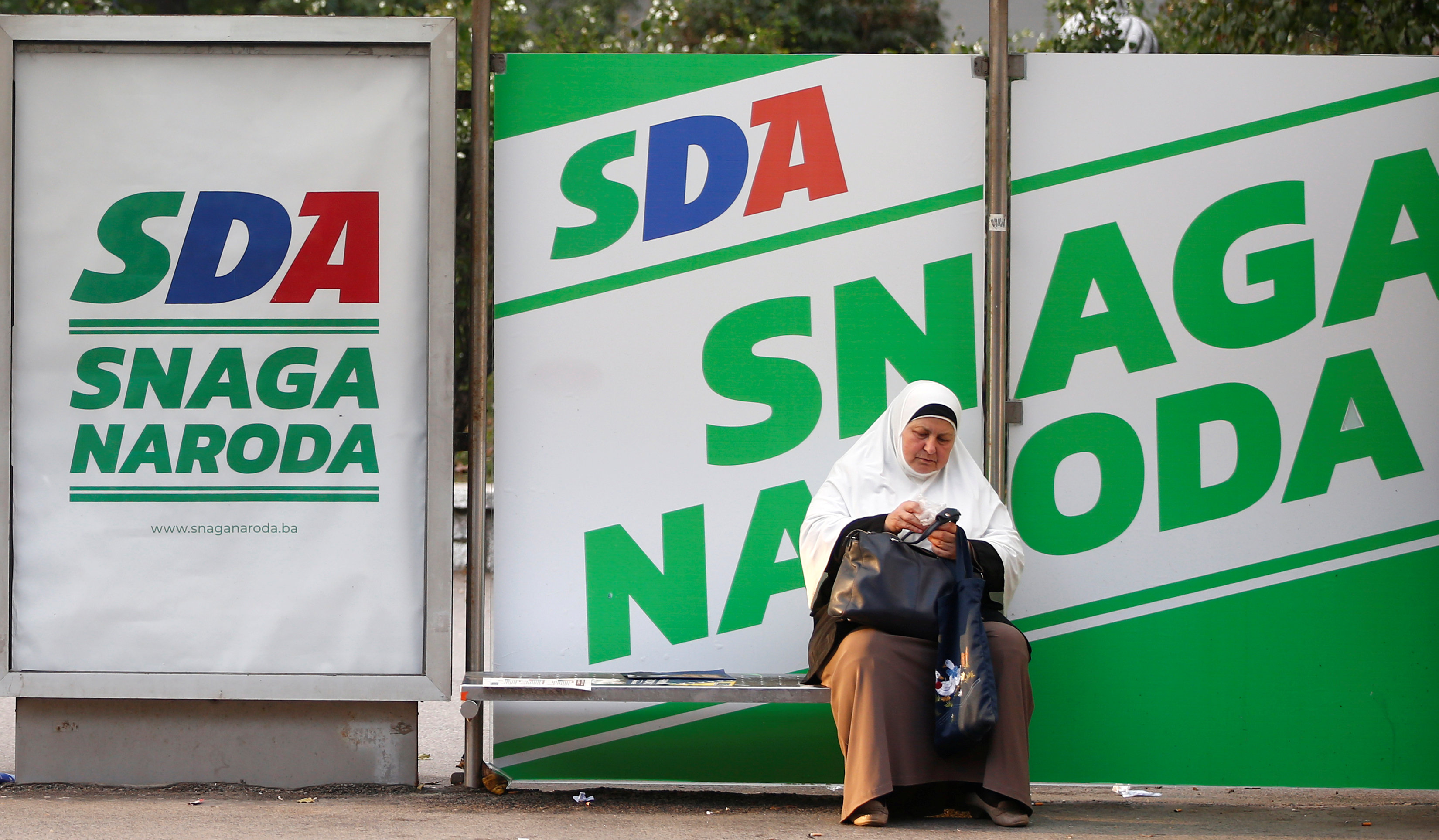 سيدة تجلس أمام أحد اللافتات فى شوارع البوسنة